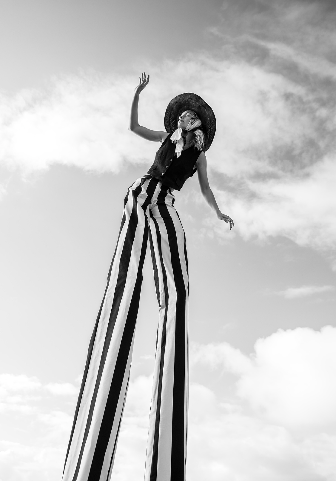 Black and white fashion photo of model in striped wide-leg pants and wide-brim hat against sky.