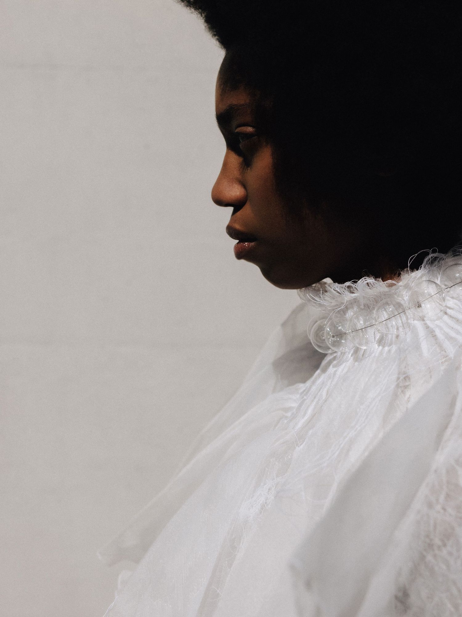 Elegant side profile of model in white ruffled tulle collar against light grey background.