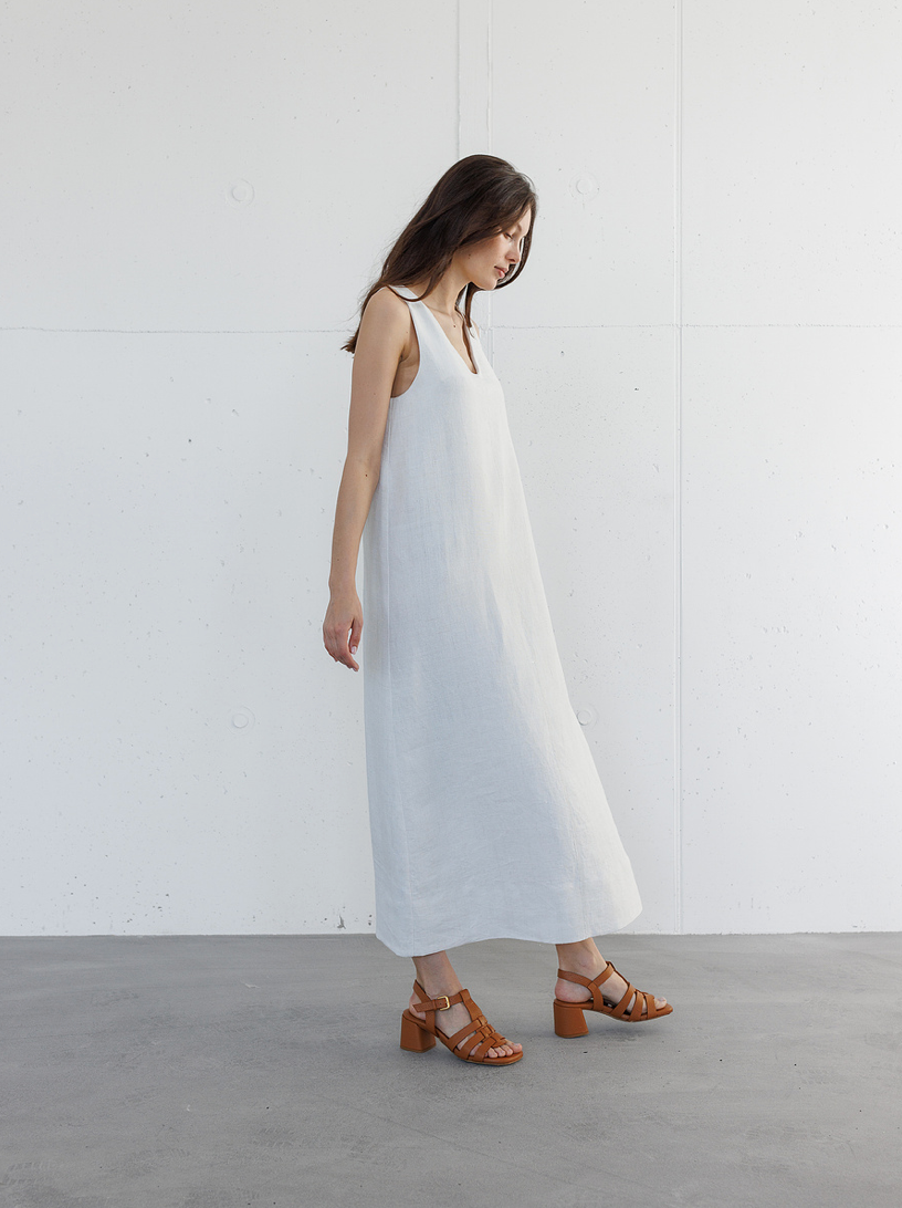 Woman modeling a minimalist white sleeveless maxi dress paired with tan strappy block heel sandals.
