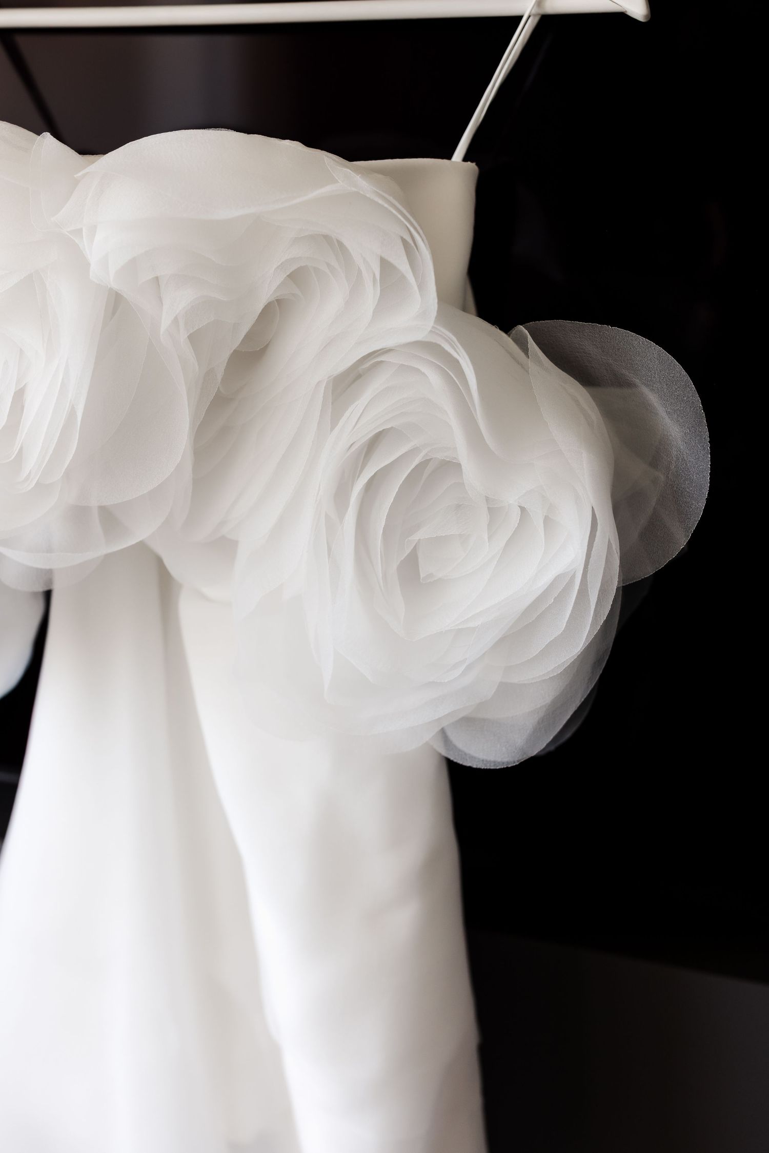 Close-up of a white wedding dress with elegant ruffled organza rose details hanging on a hanger.