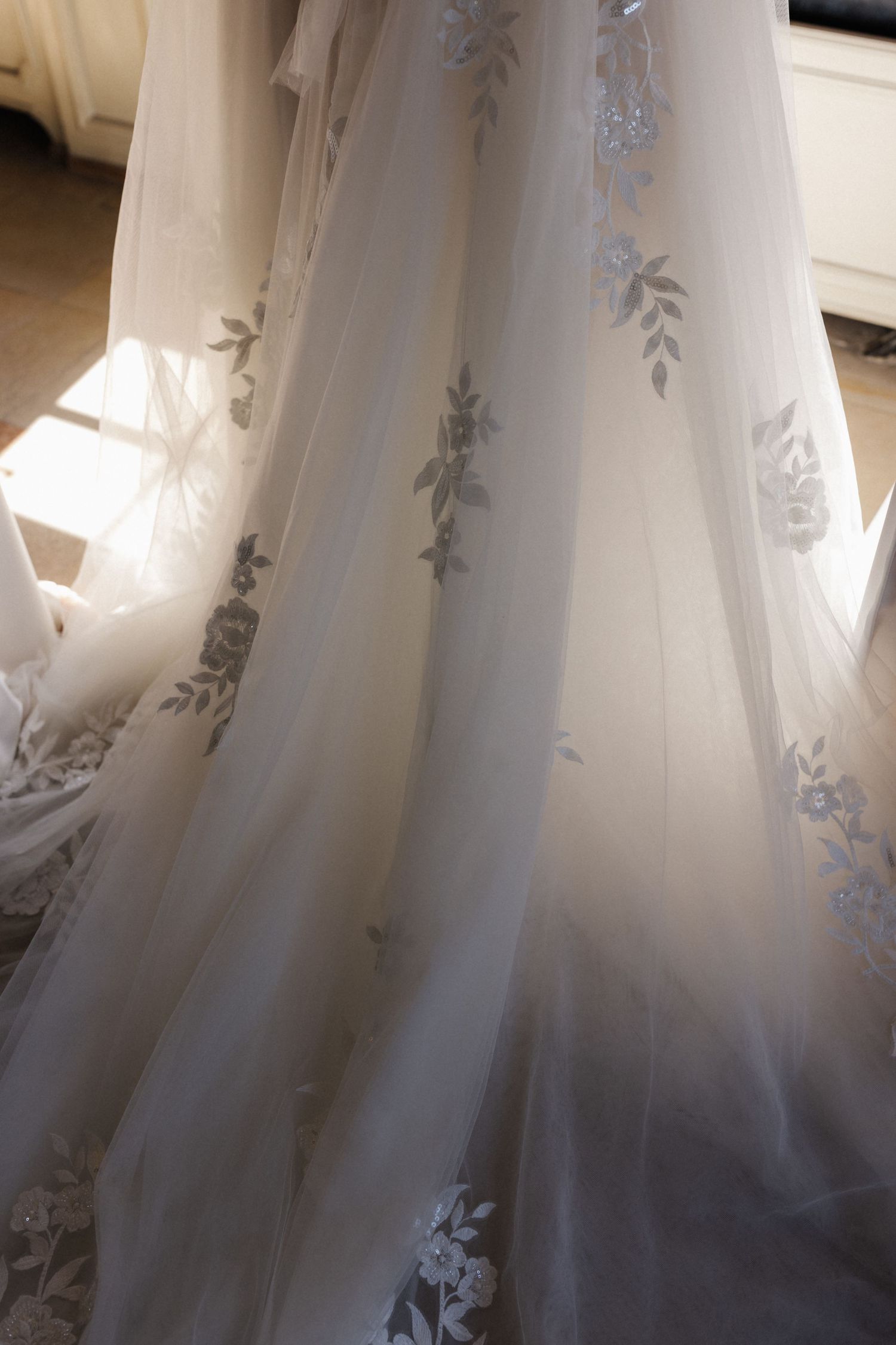 Close-up of a flowing bridal gown with delicate blue floral and leaf embroidery on sheer tulle.