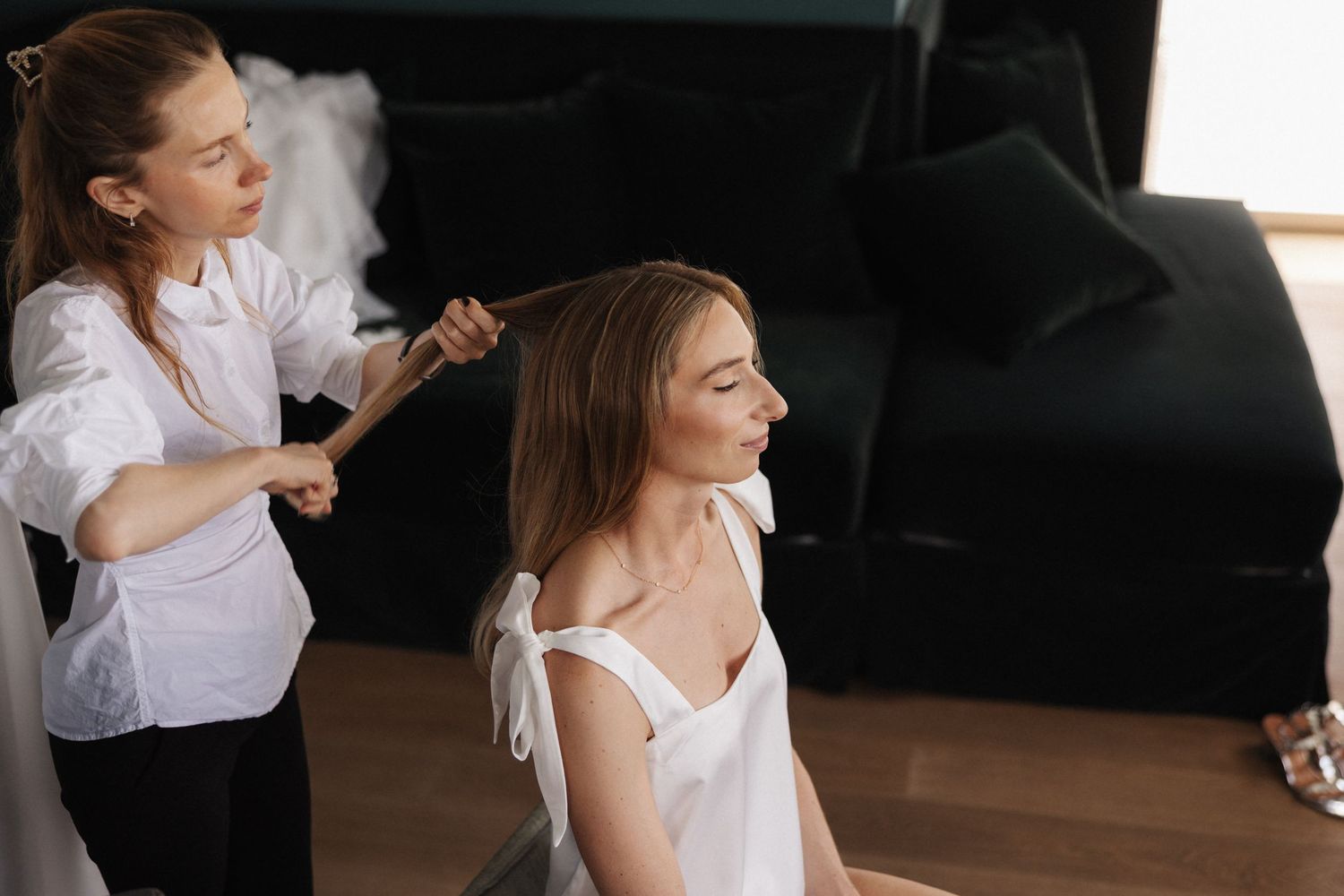 Hairstylist straightening brides hair in bright modern hotel room.