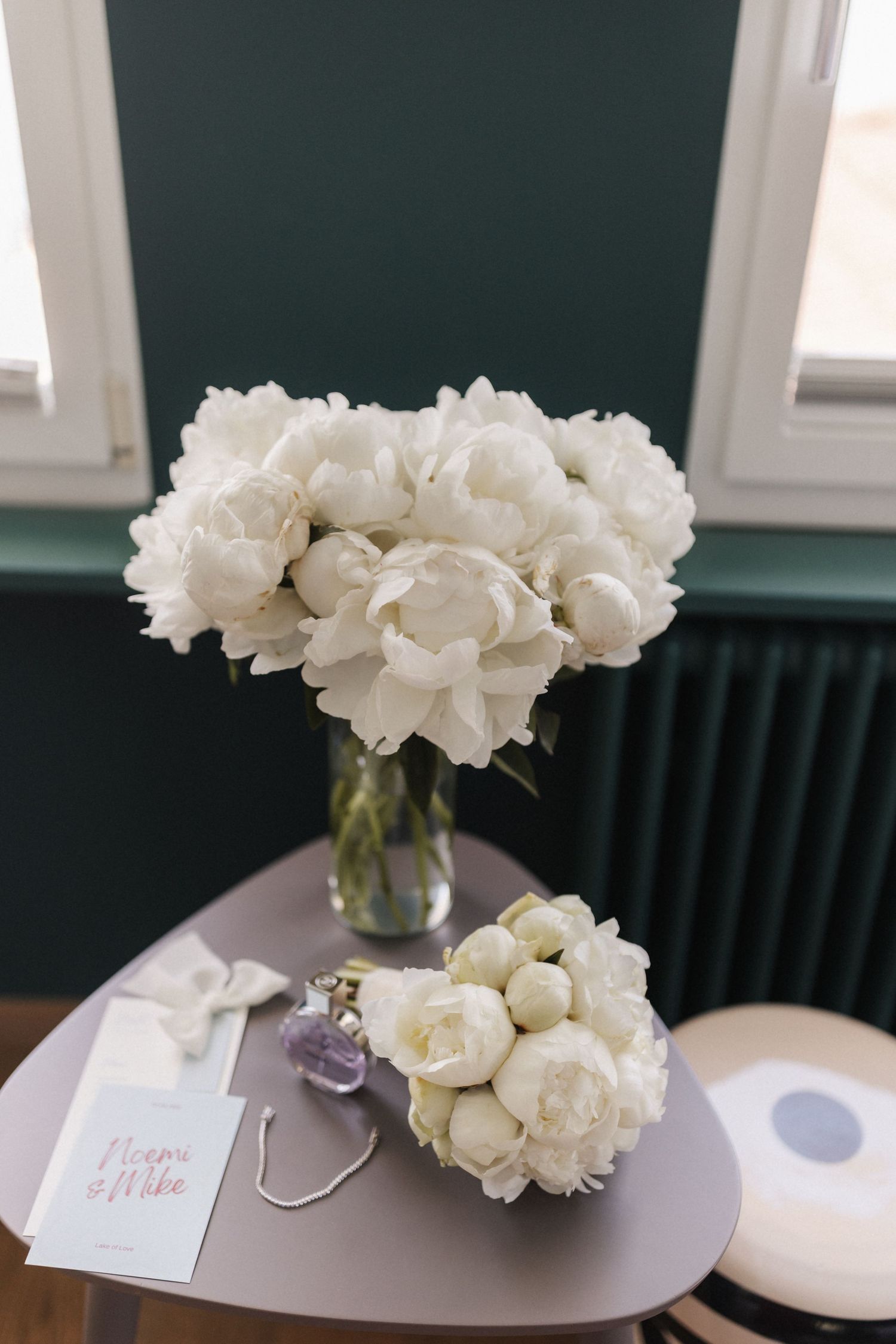 Elegant white peony bouquets displayed on a table with a handwritten card and jewelry.