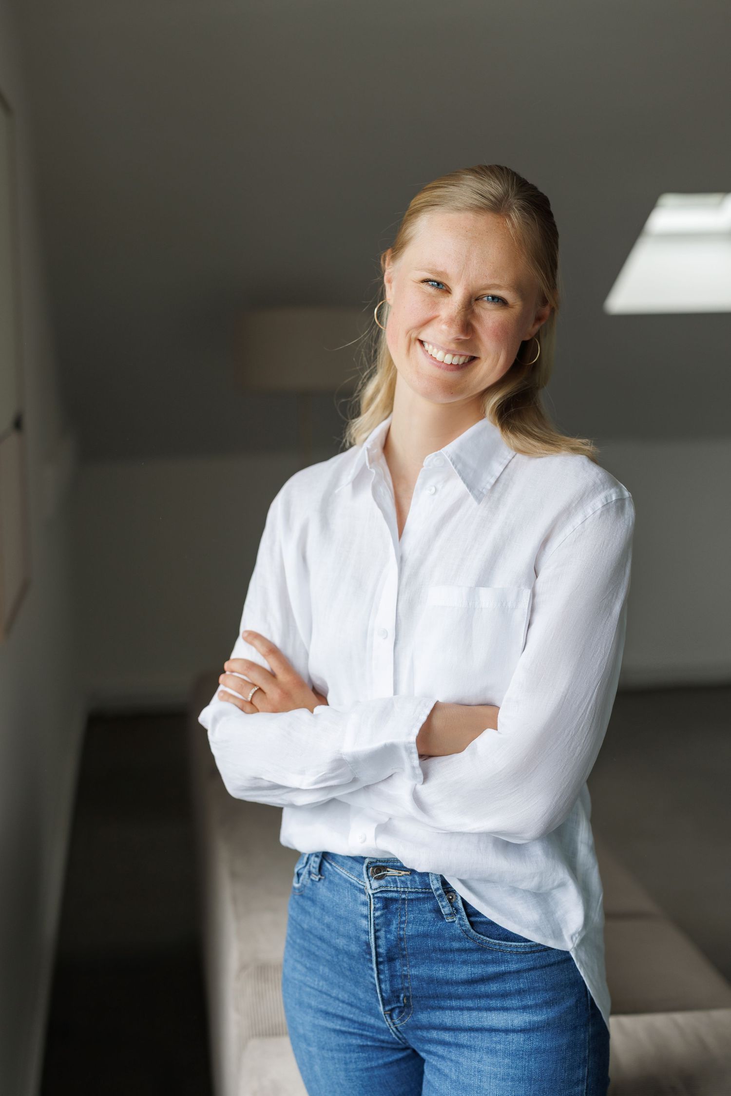 Confident blonde woman in white shirt and jeans standing with arms crossed, smiling.