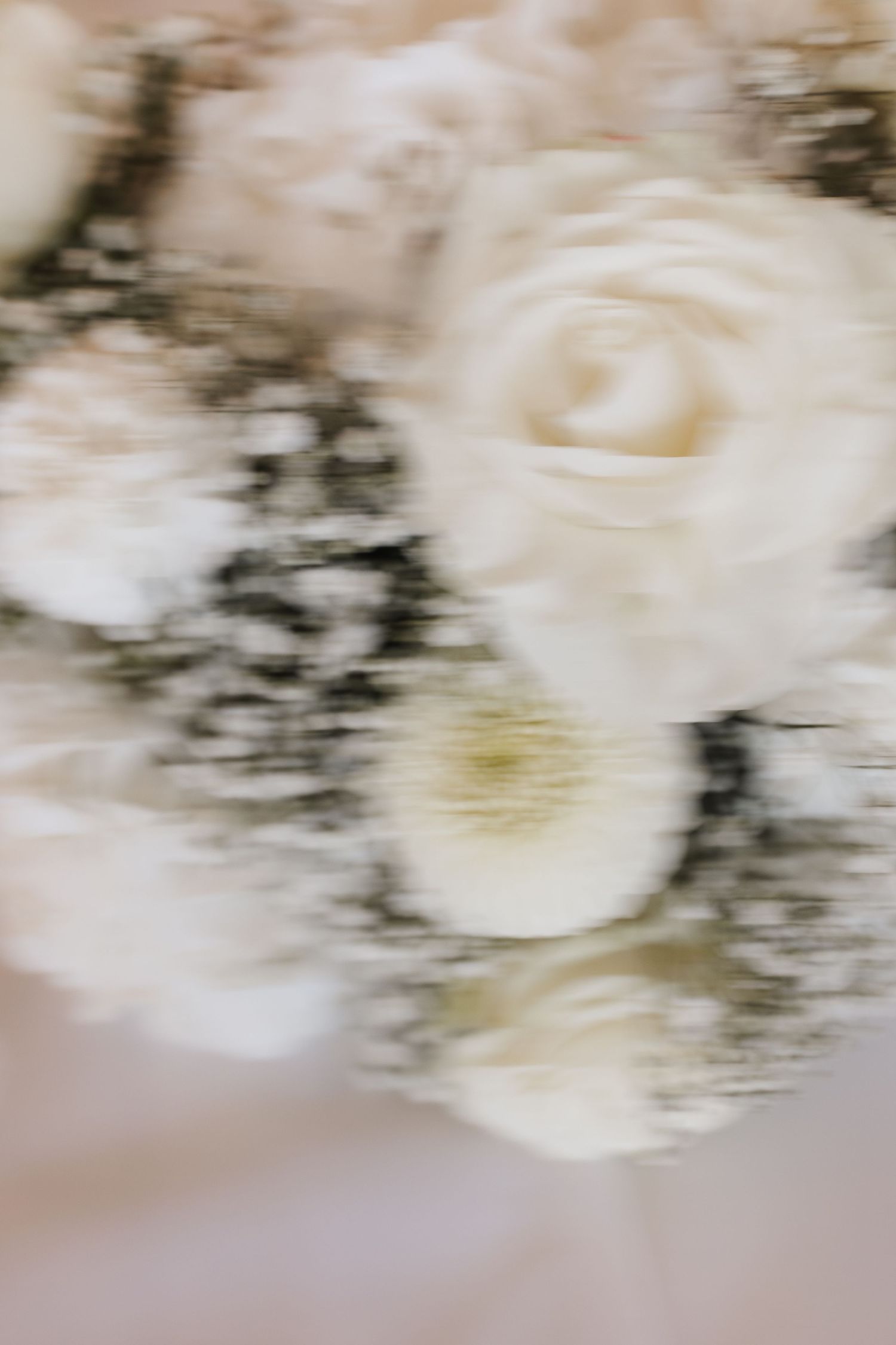 Close-up blurred artistic shot of white wedding bouquet featuring roses, dahlias, and delicate baby's breath flowers.