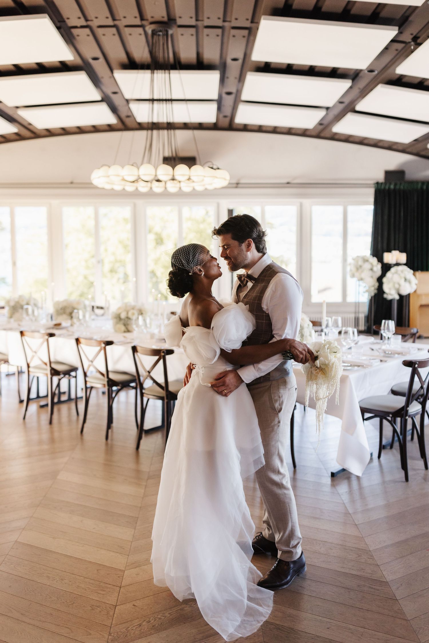 Interracial couple sharing romantic moment in elegant wedding reception hall with herringbone floors.