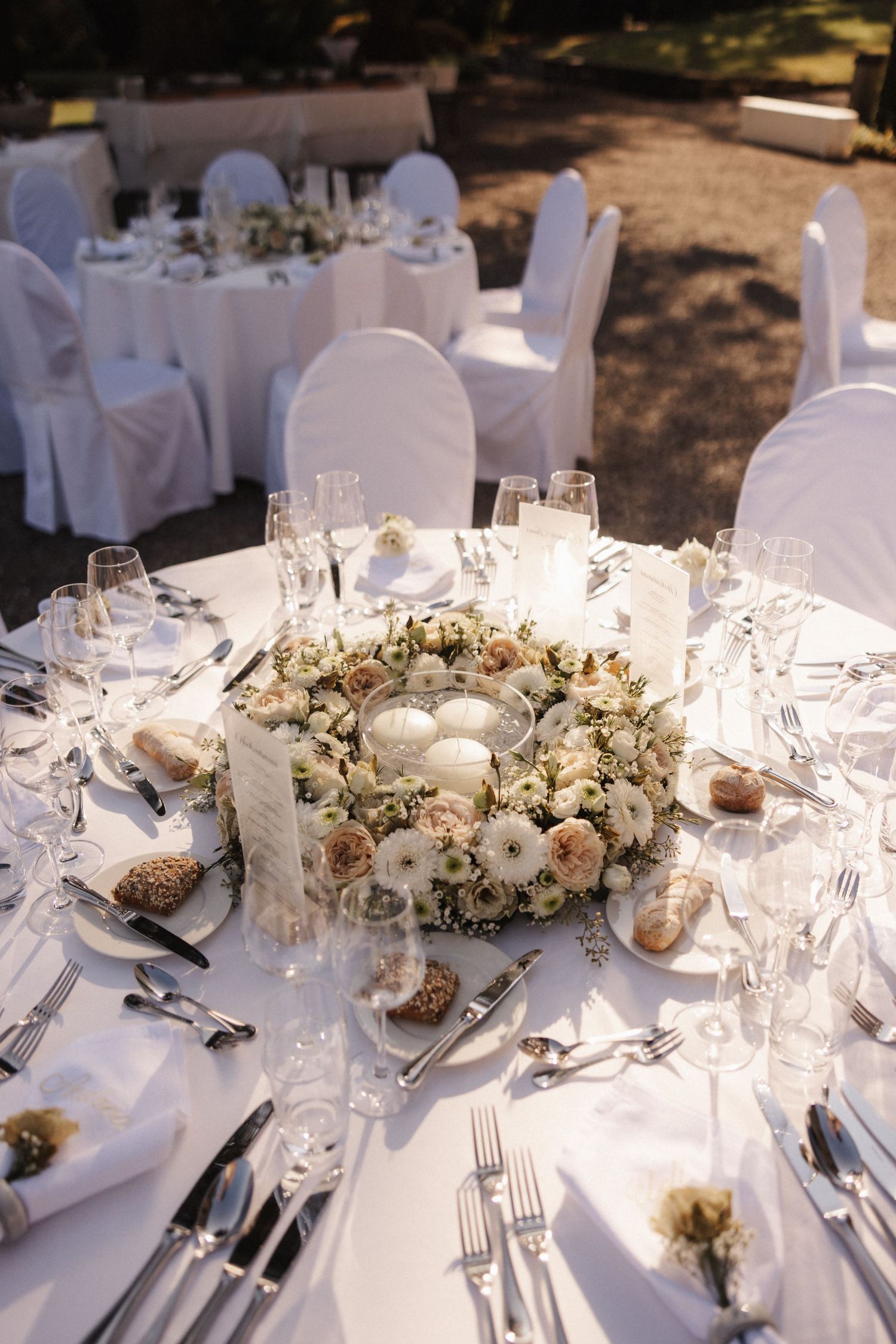 Elegant outdoor wedding reception with round tables, white floral centerpieces, and floating candles.