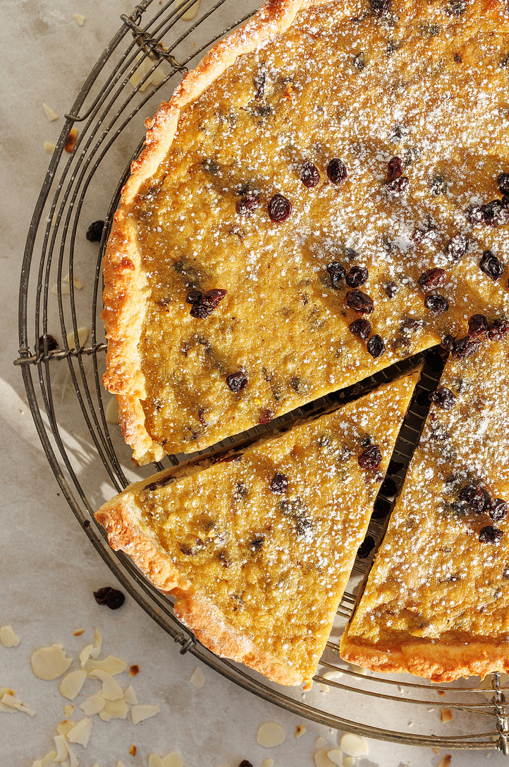 Overhead view of a golden tart with raisins and powdered sugar on a wire cooling rack.