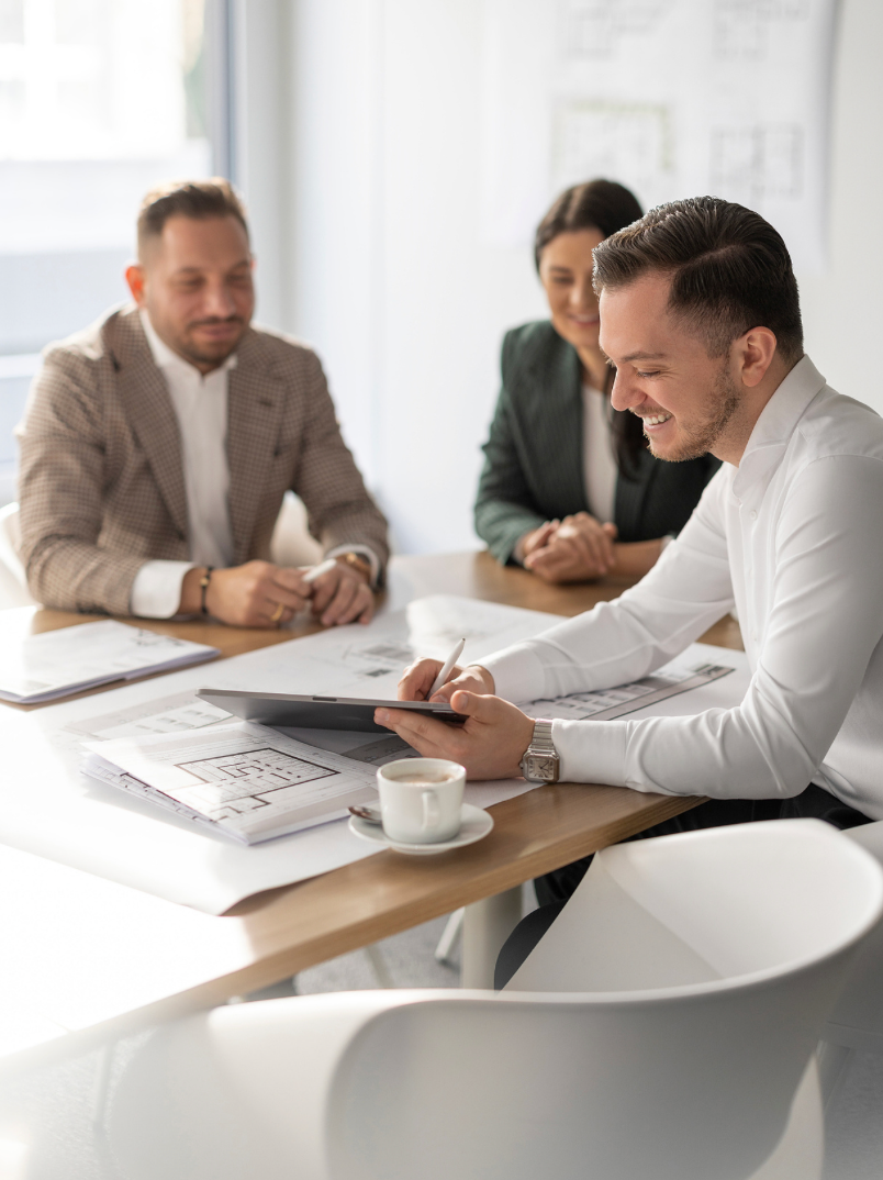Business professionals smiling and reviewing architectural plans and documents during an office meeting.