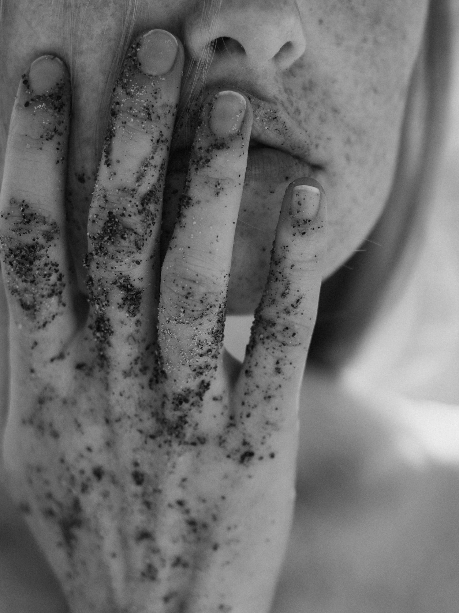Black and white close-up of a hand covered in dark scrub touching a freckled face.