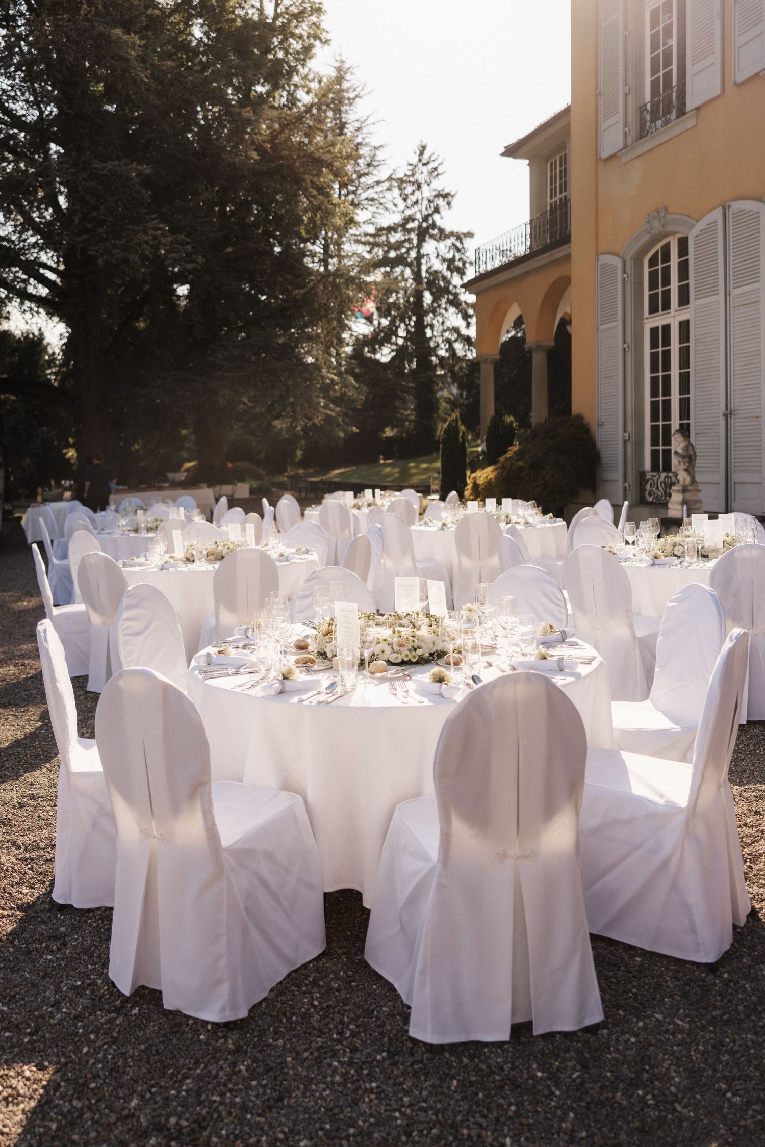 Elegant outdoor wedding reception setup with round tables draped in white linens and white chair covers at a villa.
