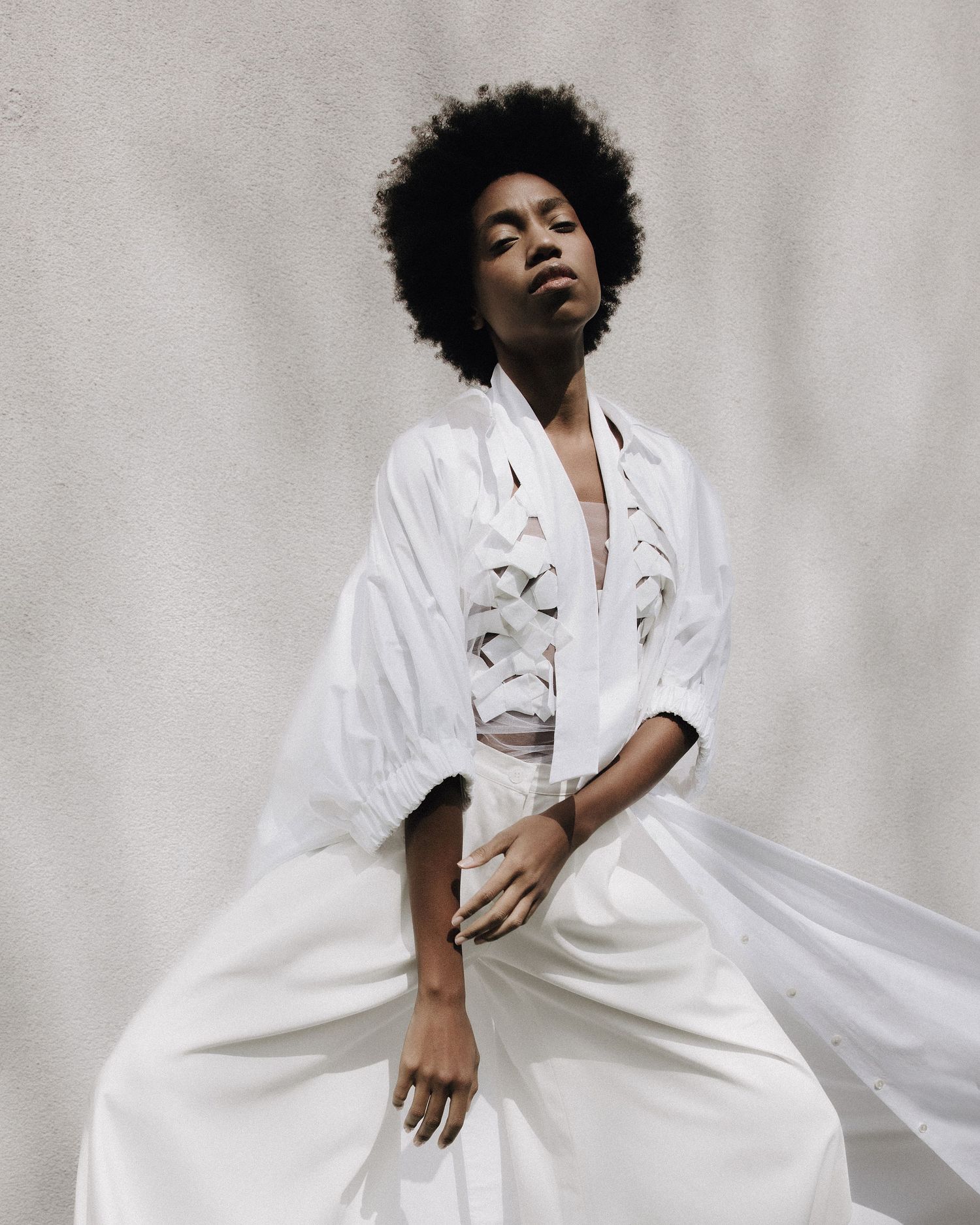 Model in flowing white oversized lace-up dress with natural afro hairstyle poses gracefully.