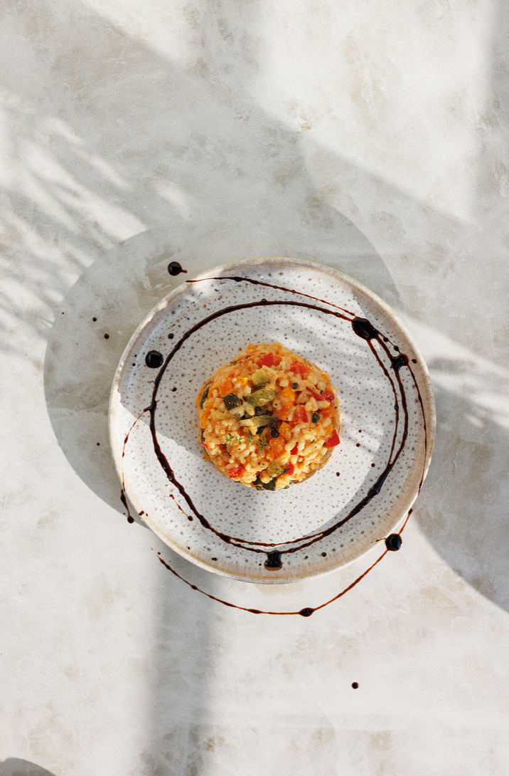 Overhead view of a vegetable risotto on a speckled ceramic plate with balsamic drizzle.