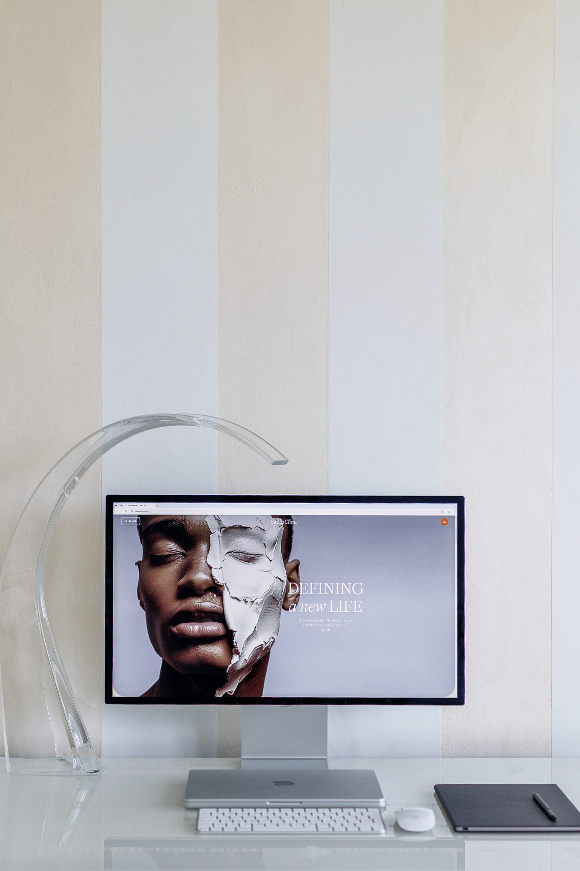 A desktop computer monitor displays a beauty website on a sleek white desk with a modern lamp.
