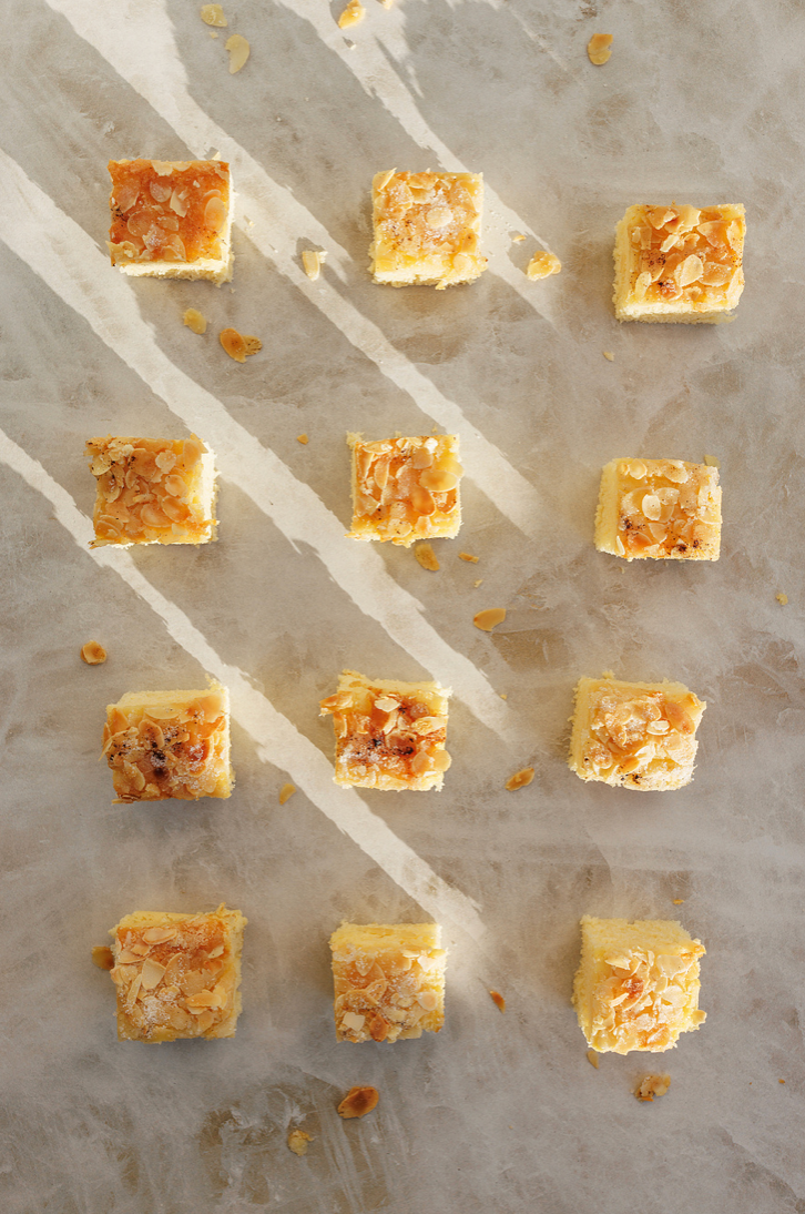 Twelve square almond caramel shortbread bars arranged in rows on a marble surface.