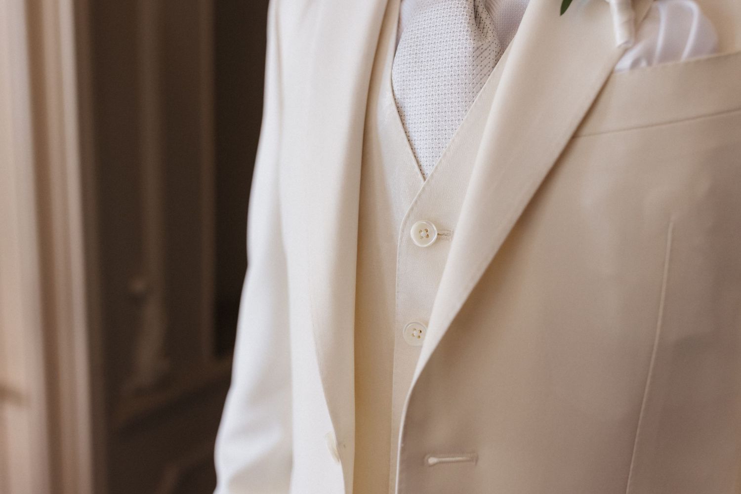Detail shot of elegant ivory wedding suit jacket with vest and white button detail.