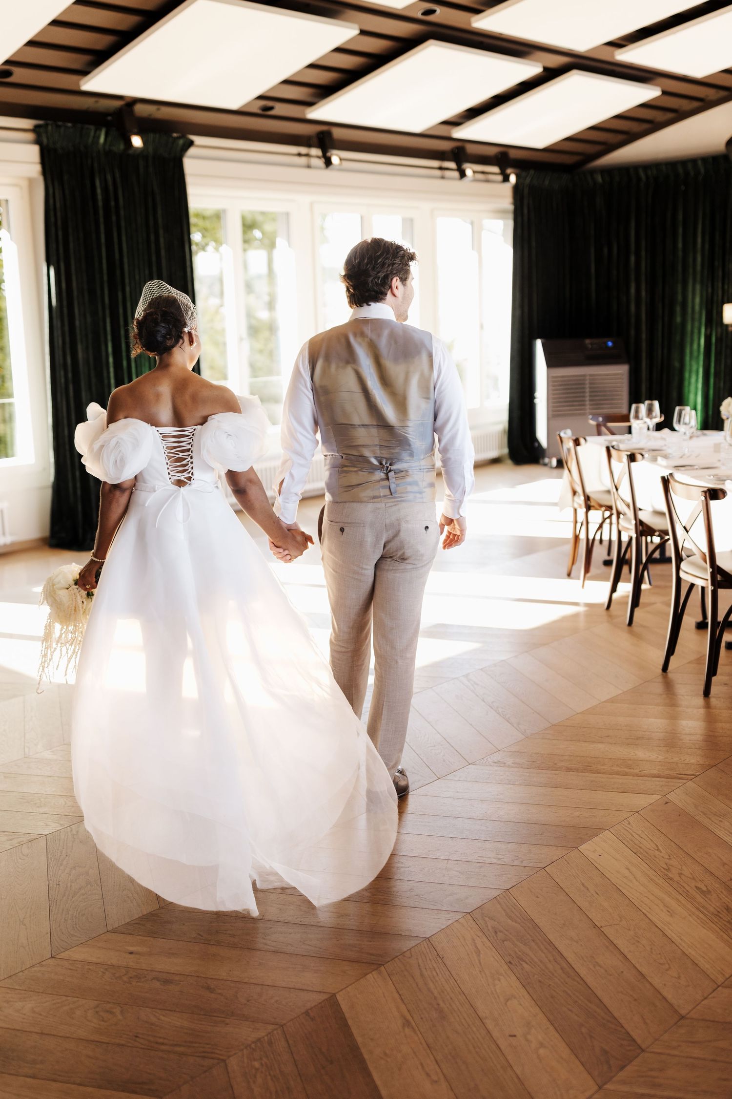 Bride and groom walking hand in hand through elegant sunlit wedding reception venue.