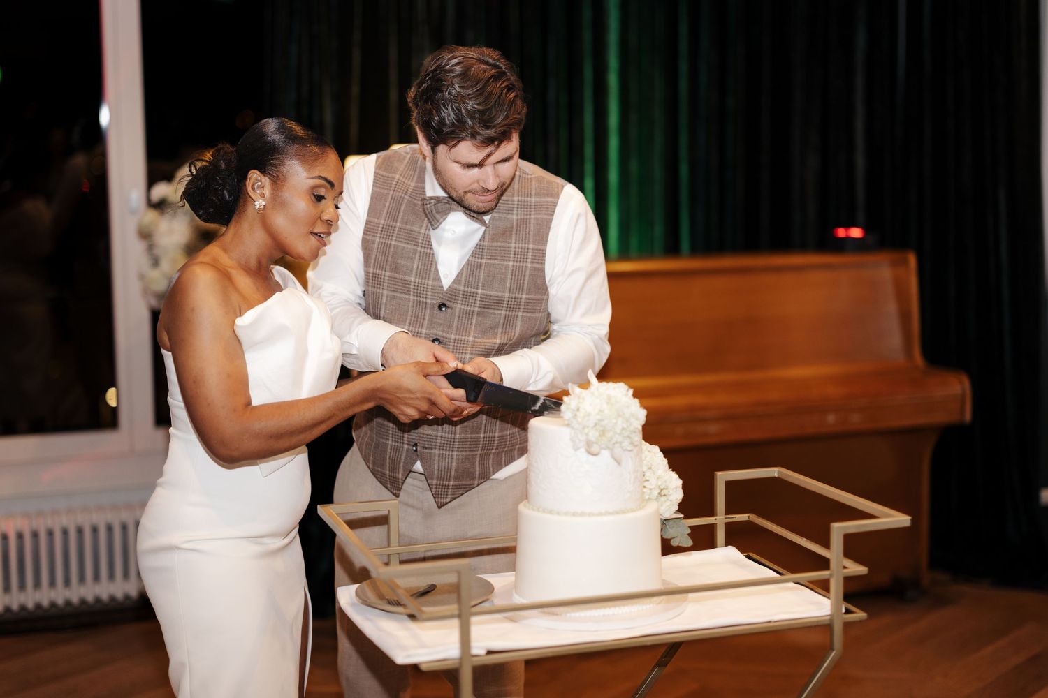 Bride and groom cutting their white wedding cake together at their elegant evening reception.