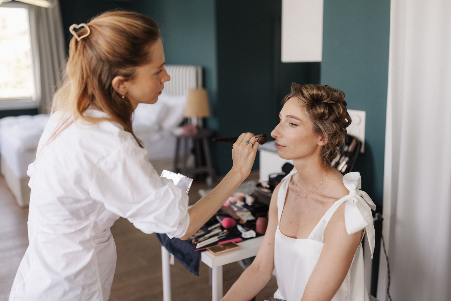 Makeup artist applying lipstick to bride with braided updo hairstyle.