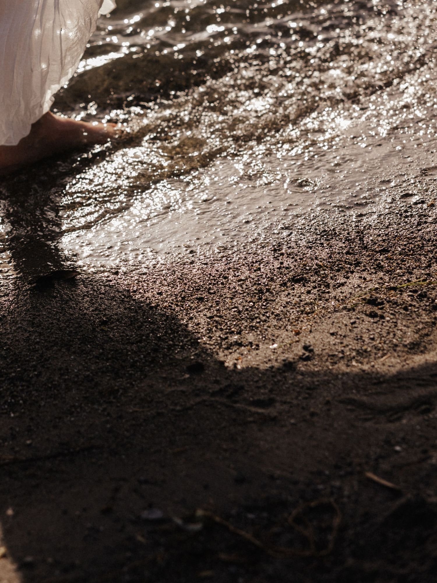 Bare feet splashing in shallow water on a wet sandy shore with sunlight reflecting off the surface.