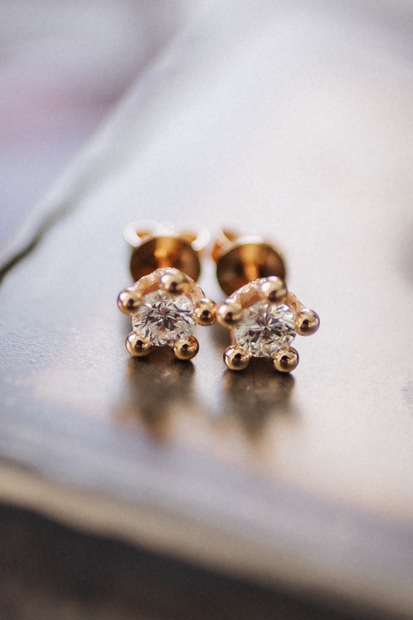 Close-up of a pair of gold diamond stud earrings resting on a reflective surface.