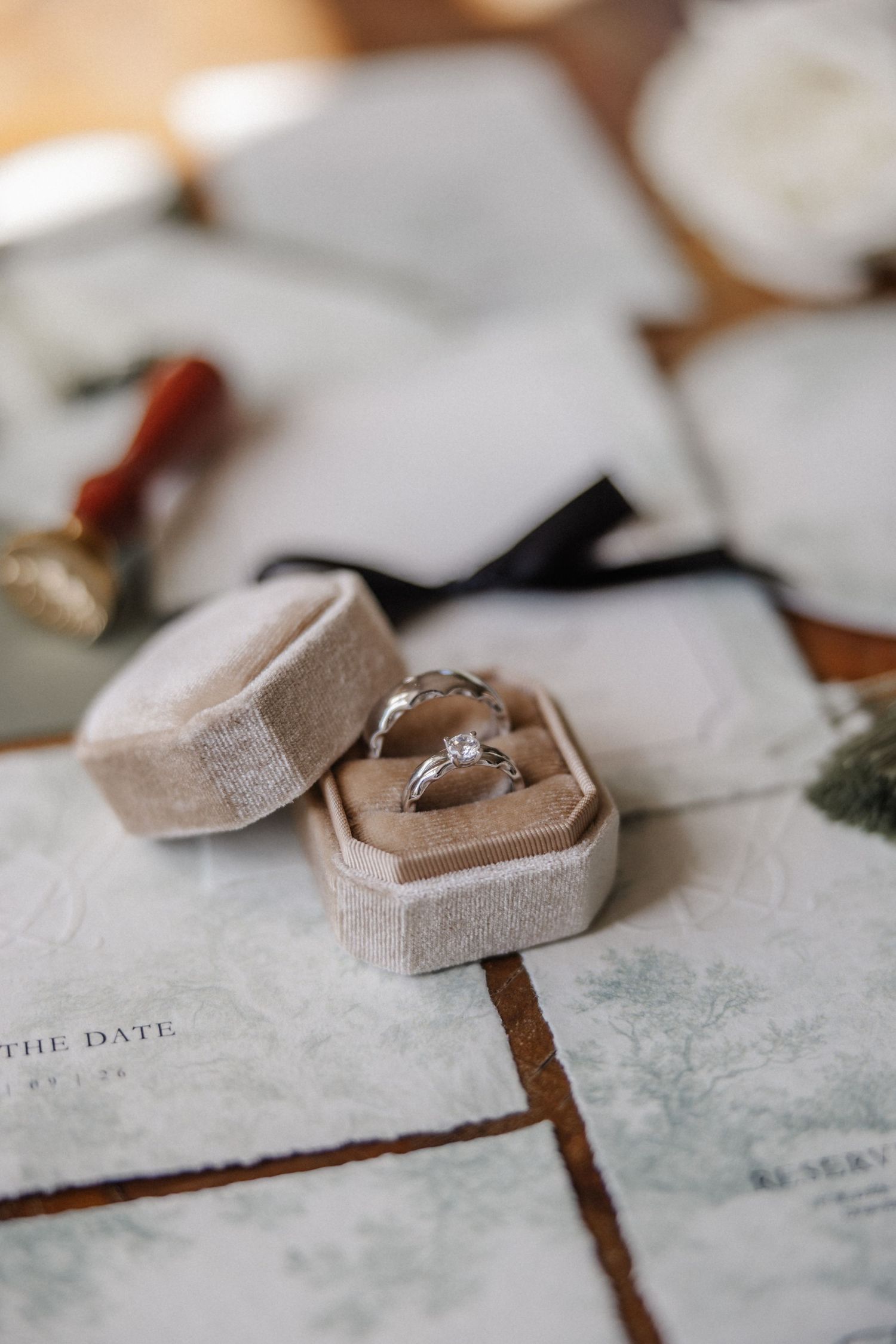 Diamond engagement ring in a beige velvet hexagonal box on elegant wedding stationery with wax seals.