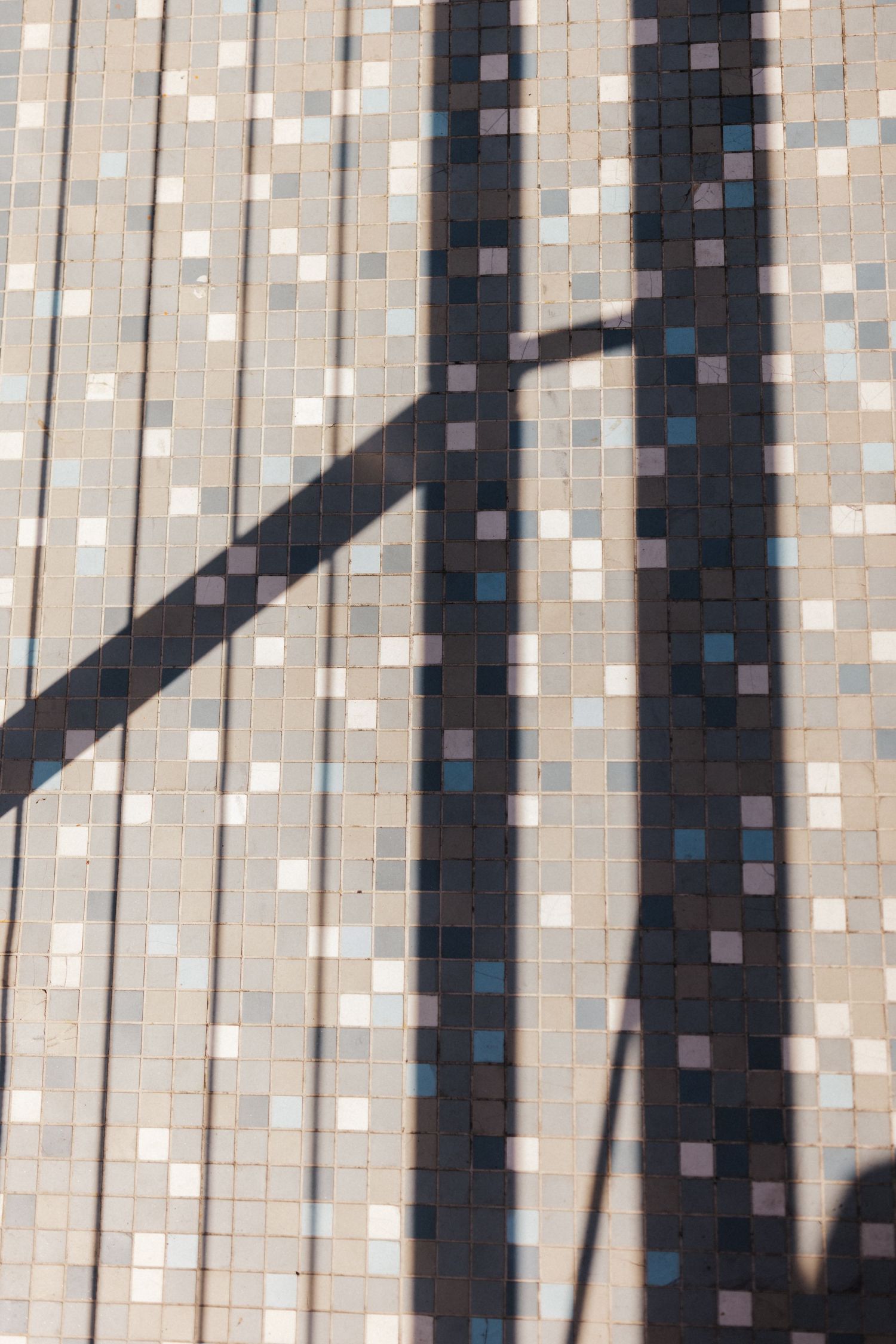 Shadow of lamp post falling diagonally across mosaic tile floor in sunlight.
