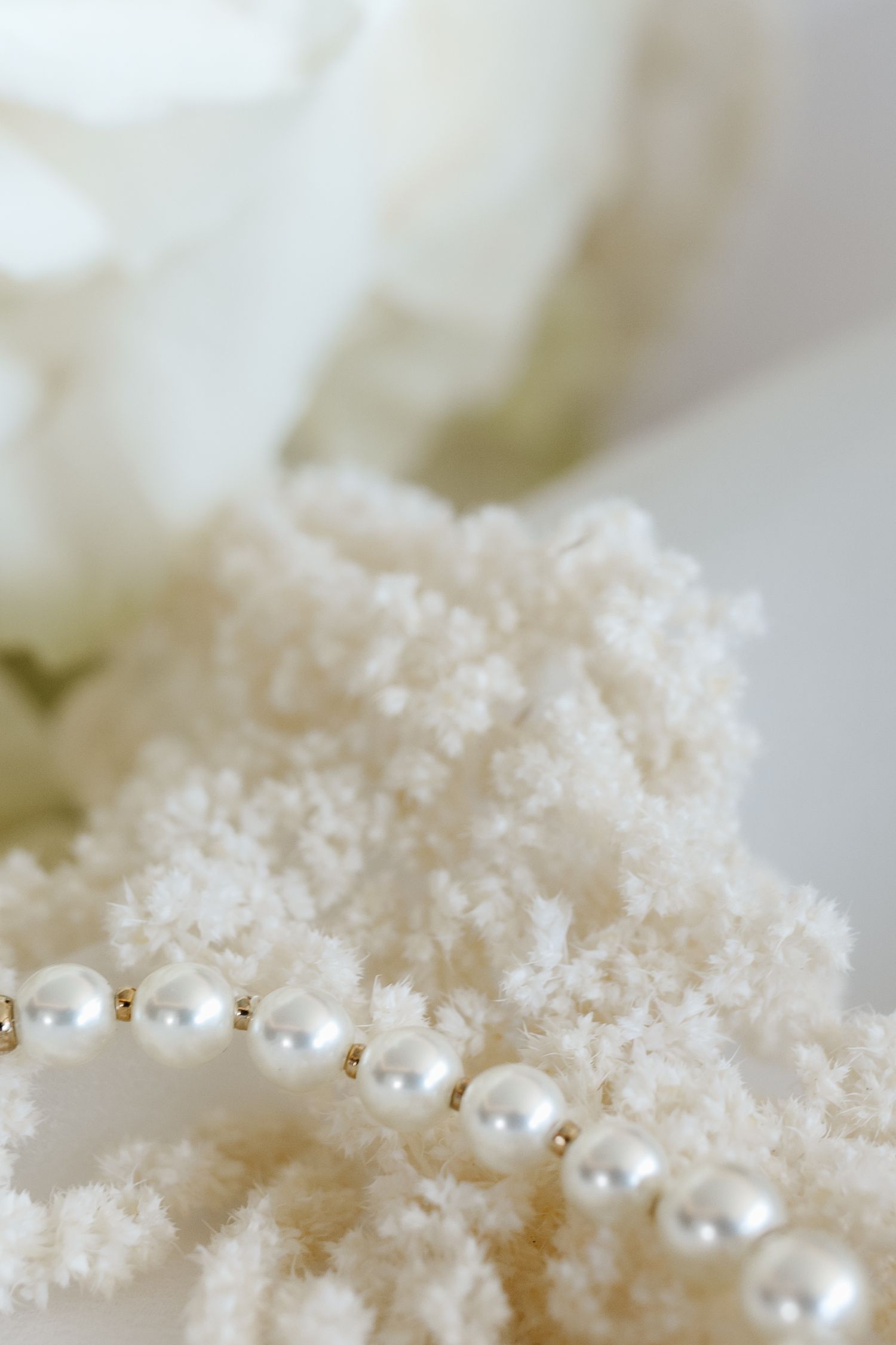 Strand of white pearls with gold spacers draped over textured ivory beaded necklace with white roses.