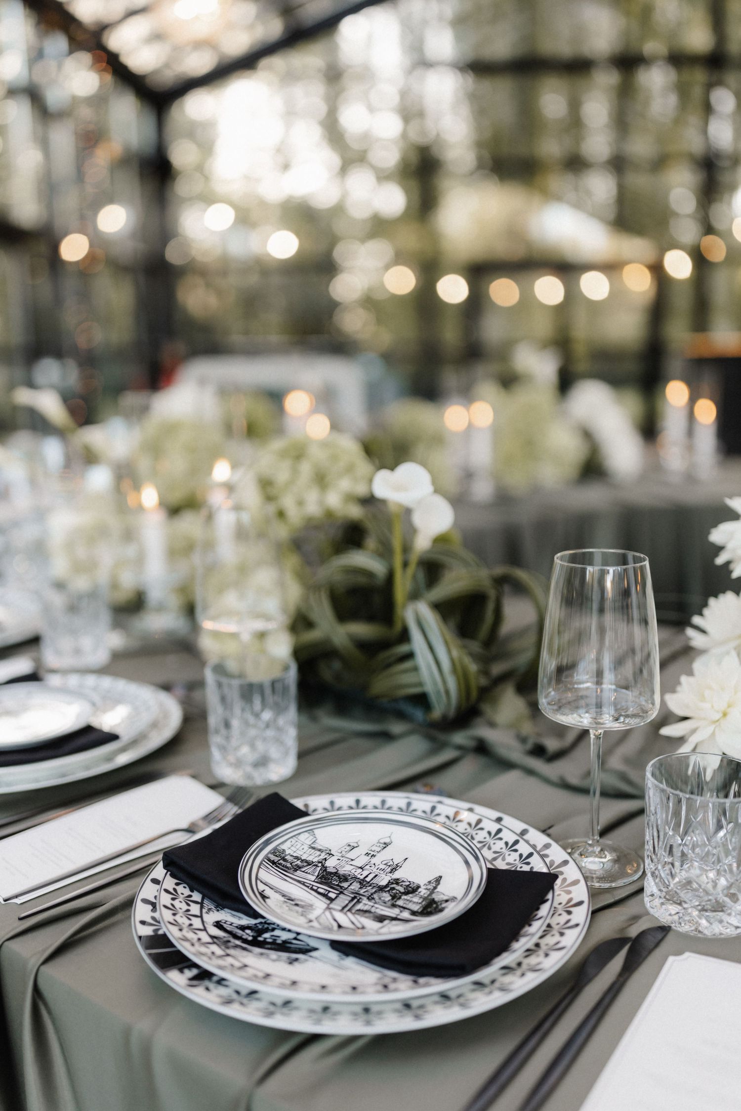 Elegant wedding table setting with black and white decorative plates, crystal glasses, and white florals.