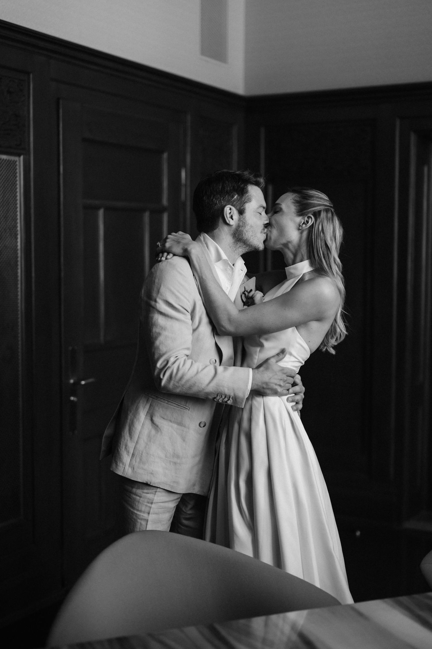 Black and white romantic photo of bride and groom sharing a kiss in elegant dark-paneled room on their wedding day.