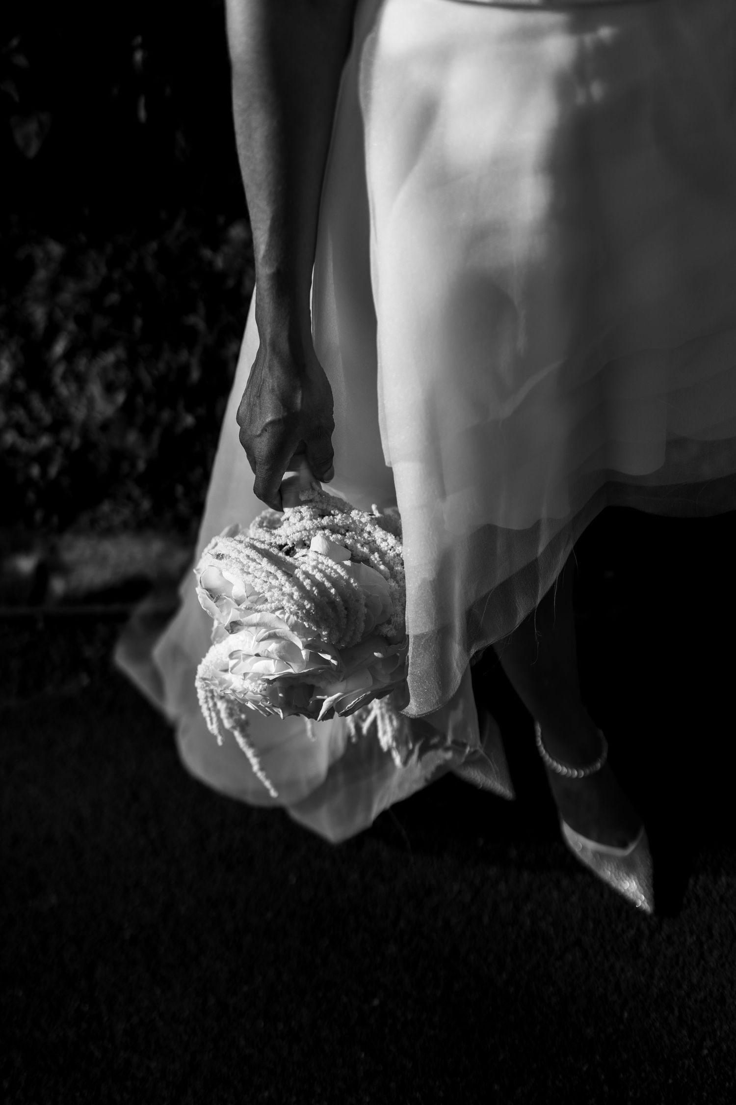 Black and white photo of a bride in a white gown holding a floral bouquet at her side while walking.