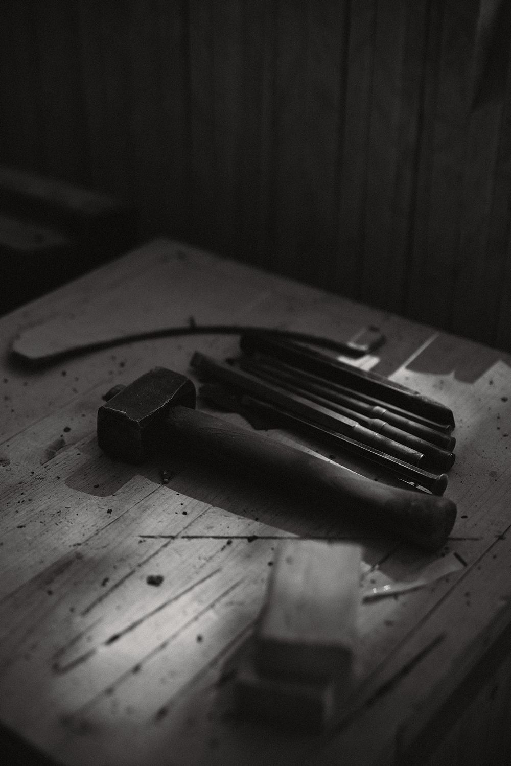 Set of chisels and a hammer arranged on a worn wooden workbench in a dark workshop.