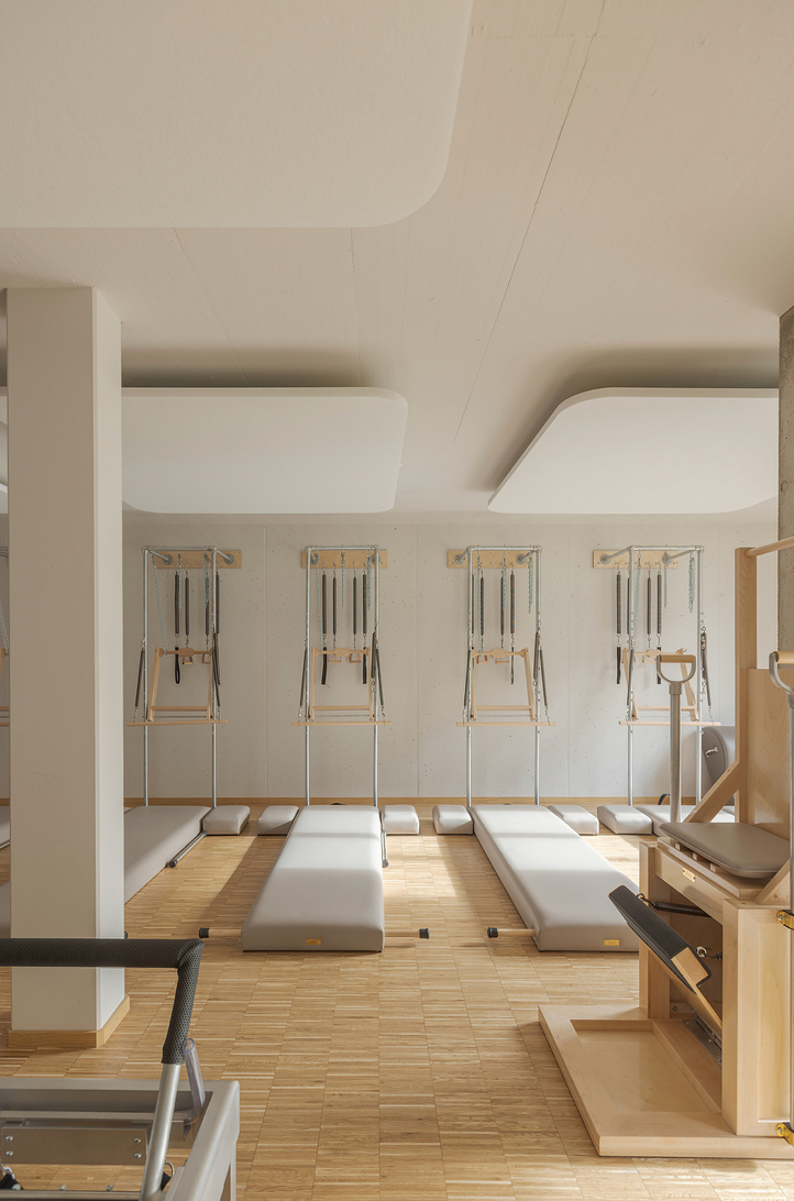 Modern Pilates studio with wooden reformers, wall-mounted cadillac towers and natural wood floors.