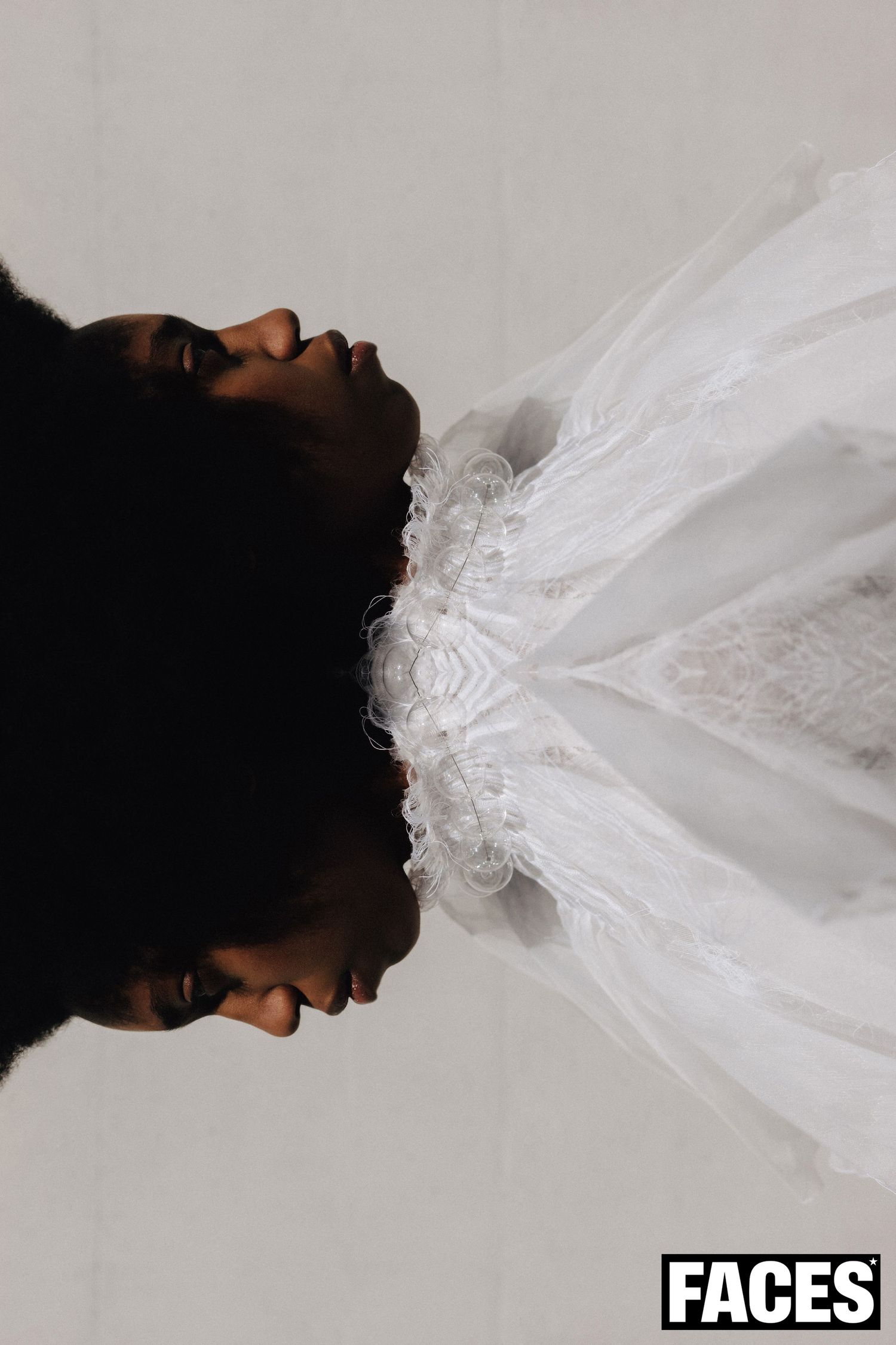 Artistic upward profile view of model with afro wearing white ruffled lace collar dress.