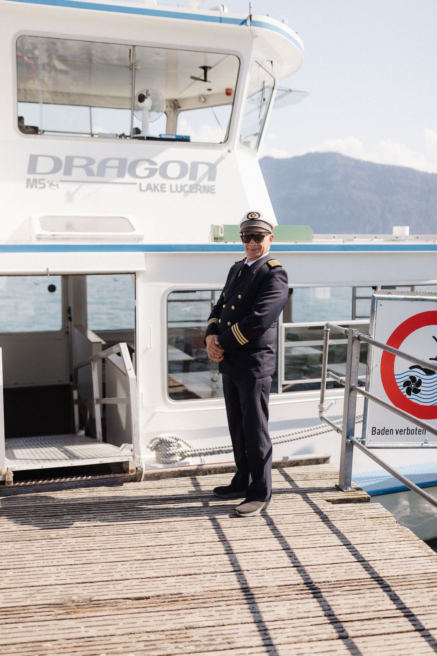 Boat captain in uniform standing on the dock beside MS Dragon vessel on Lake Lucerne.