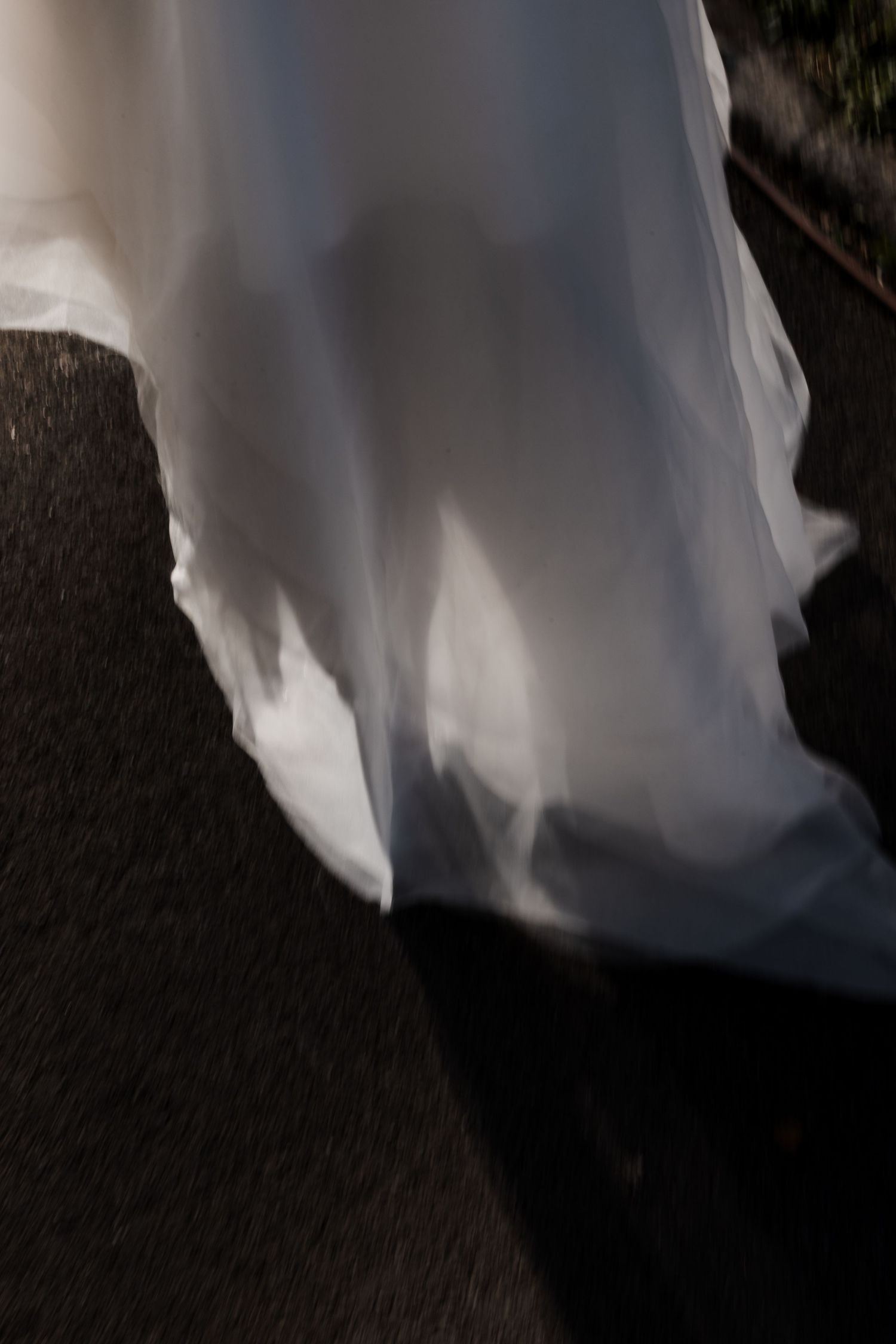 Abstract motion blur of white wedding dress train flowing on dark pavement.
