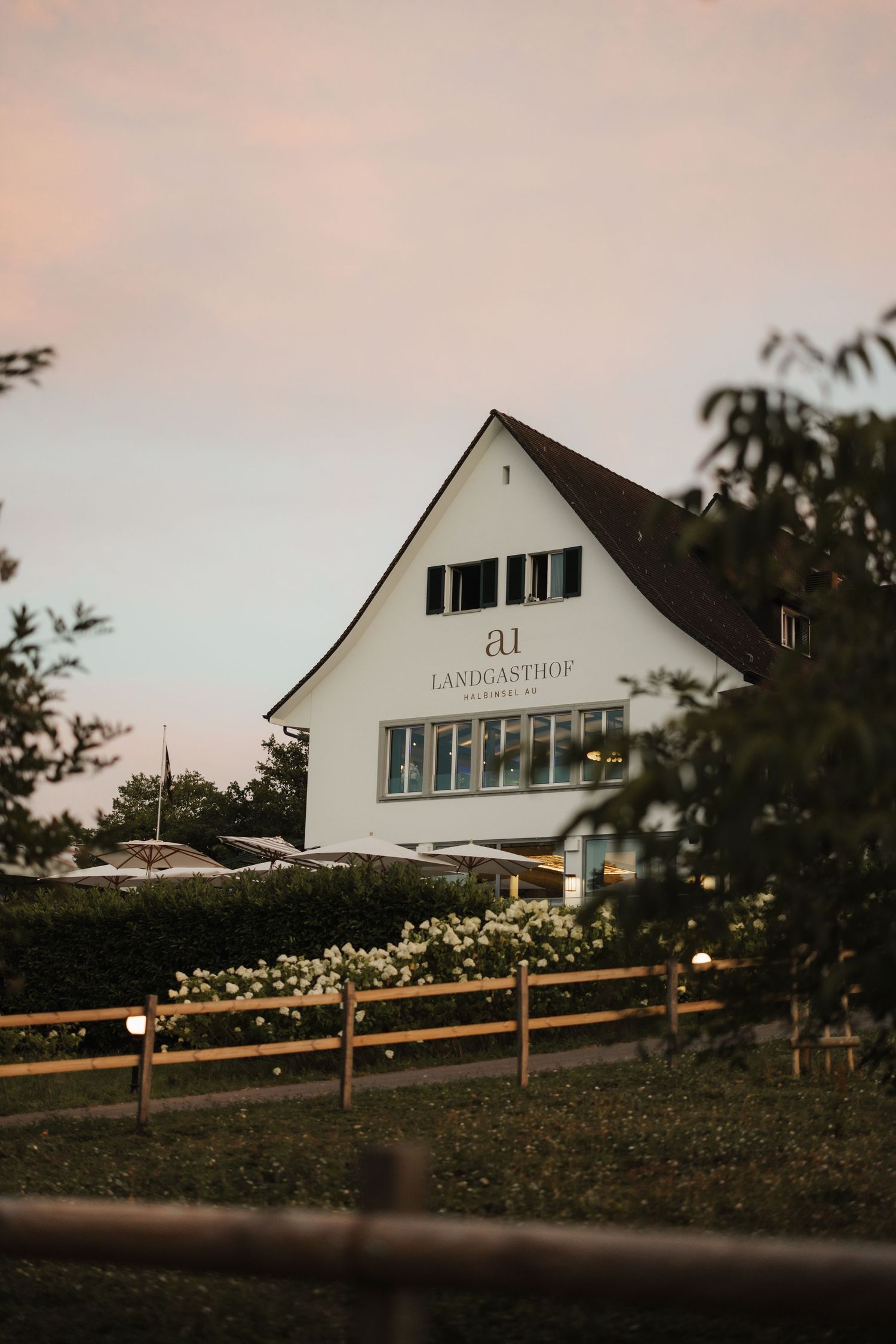 White country inn building with Landgasthof sign surrounded by greenery and flowers at dusk.