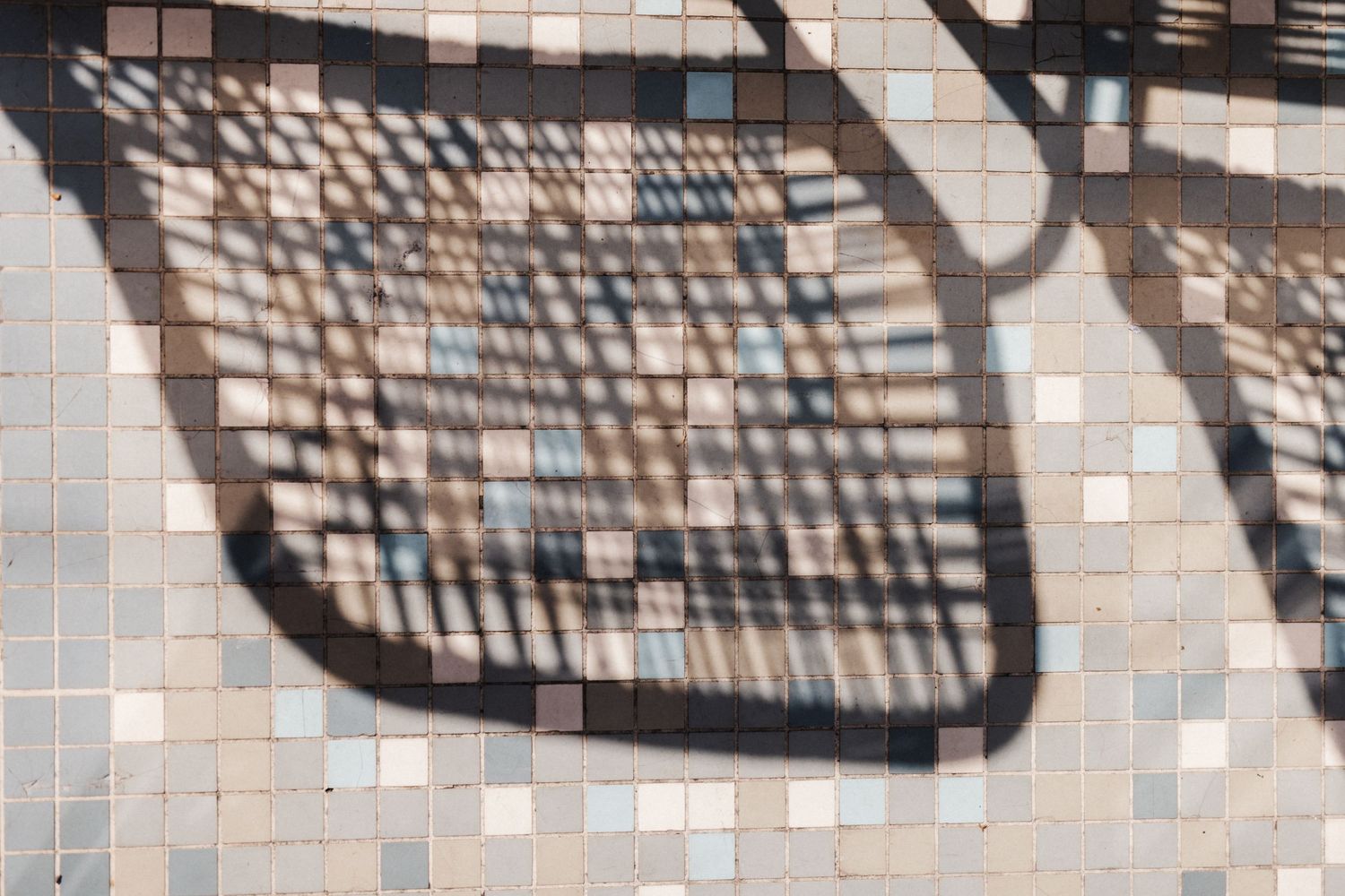 Decorative tree shadow pattern cast across colorful small square mosaic tile surface.