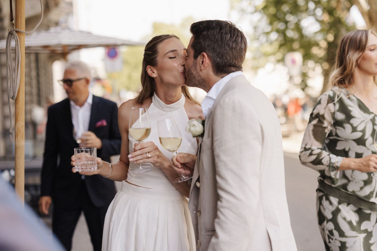 Bride and groom share a kiss while holding champagne glasses at outdoor wedding reception.
