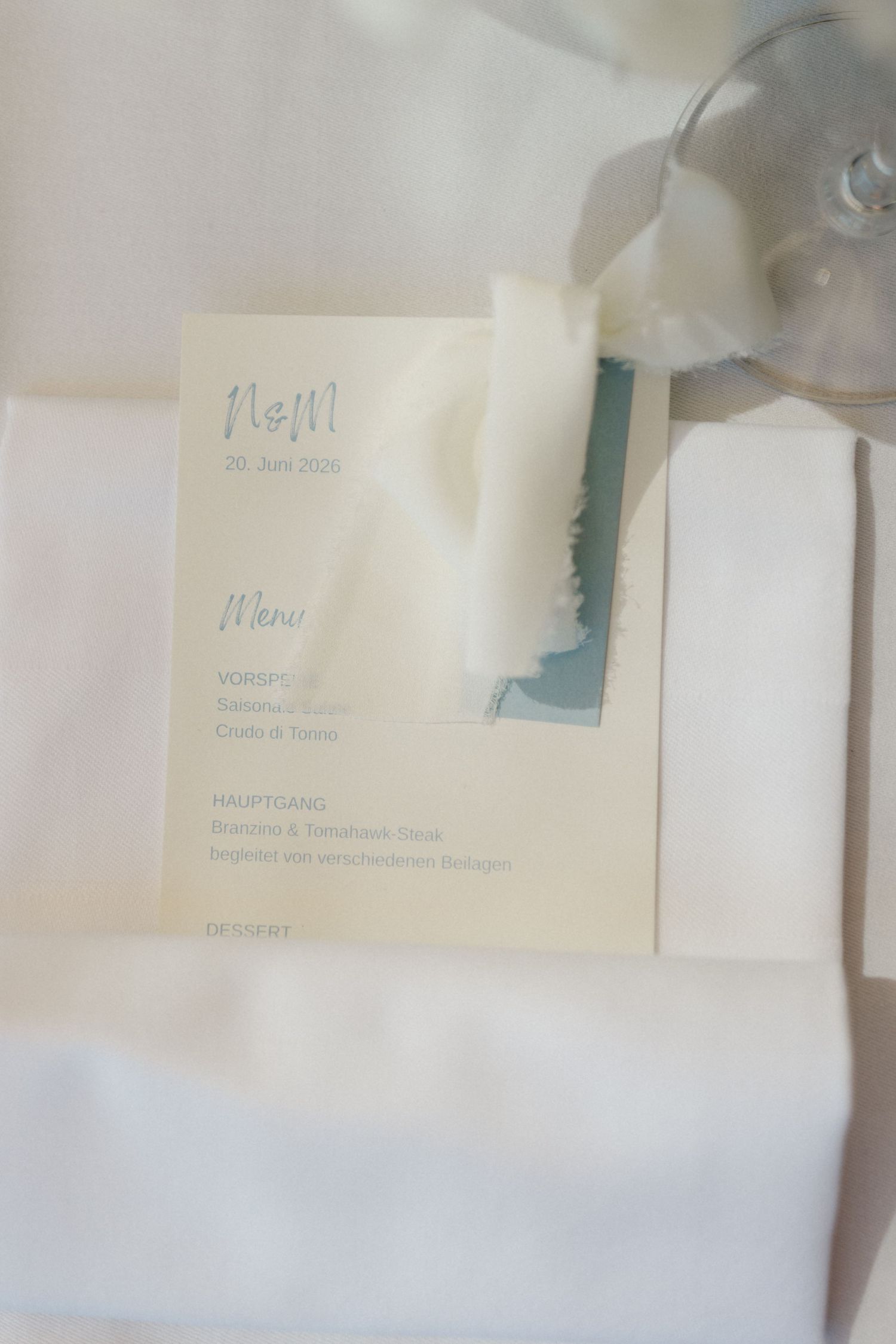 Wedding menu card with initials N&M on white linen napkin beside a crystal wine glass.