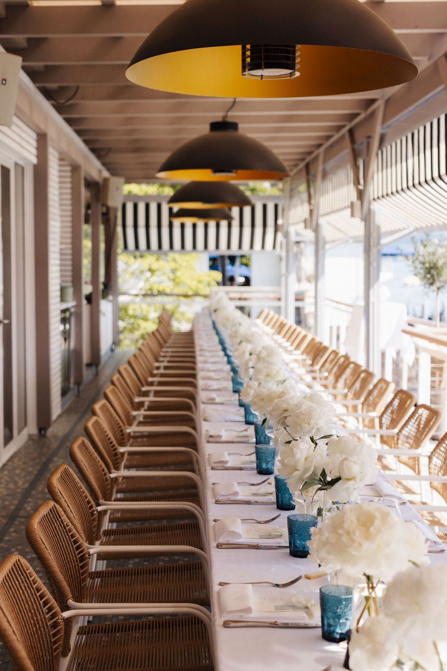 Long elegantly set wedding reception table with white hydrangeas and blue glasses under pendant lights.
