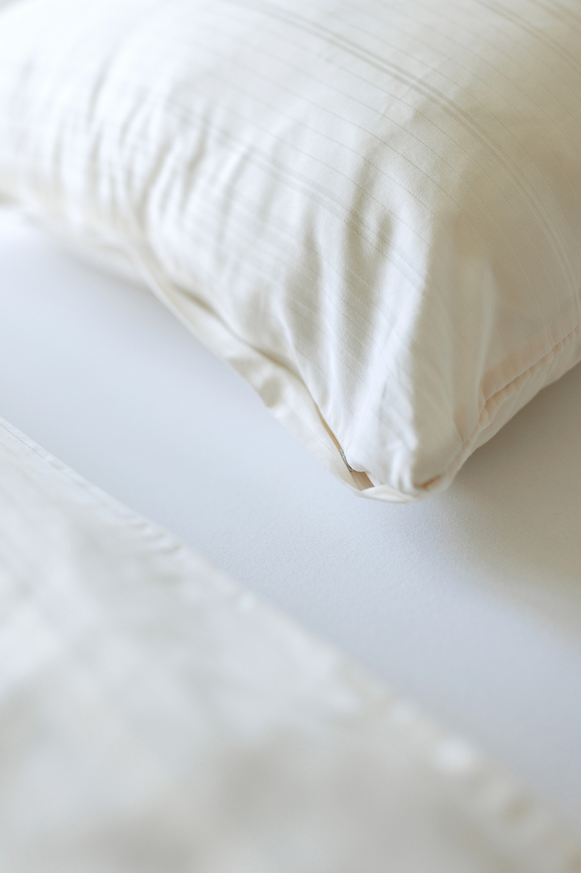 Close-up of white linen pillow and crisp bed sheets on a neatly made bed.