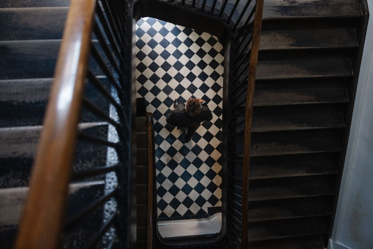 Aerial view of a spiral staircase with wooden railings and black and white checkered floor below.