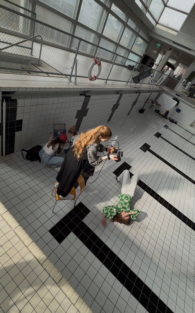 Photographer shooting a model lying on tiled floor of an indoor swimming pool facility.