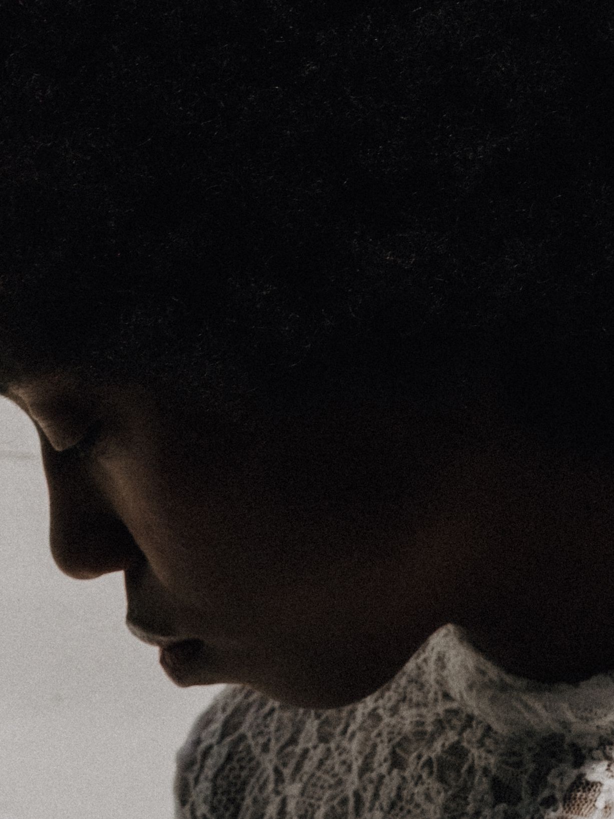 Dramatic side profile silhouette of woman with afro hair wearing delicate lace garment.