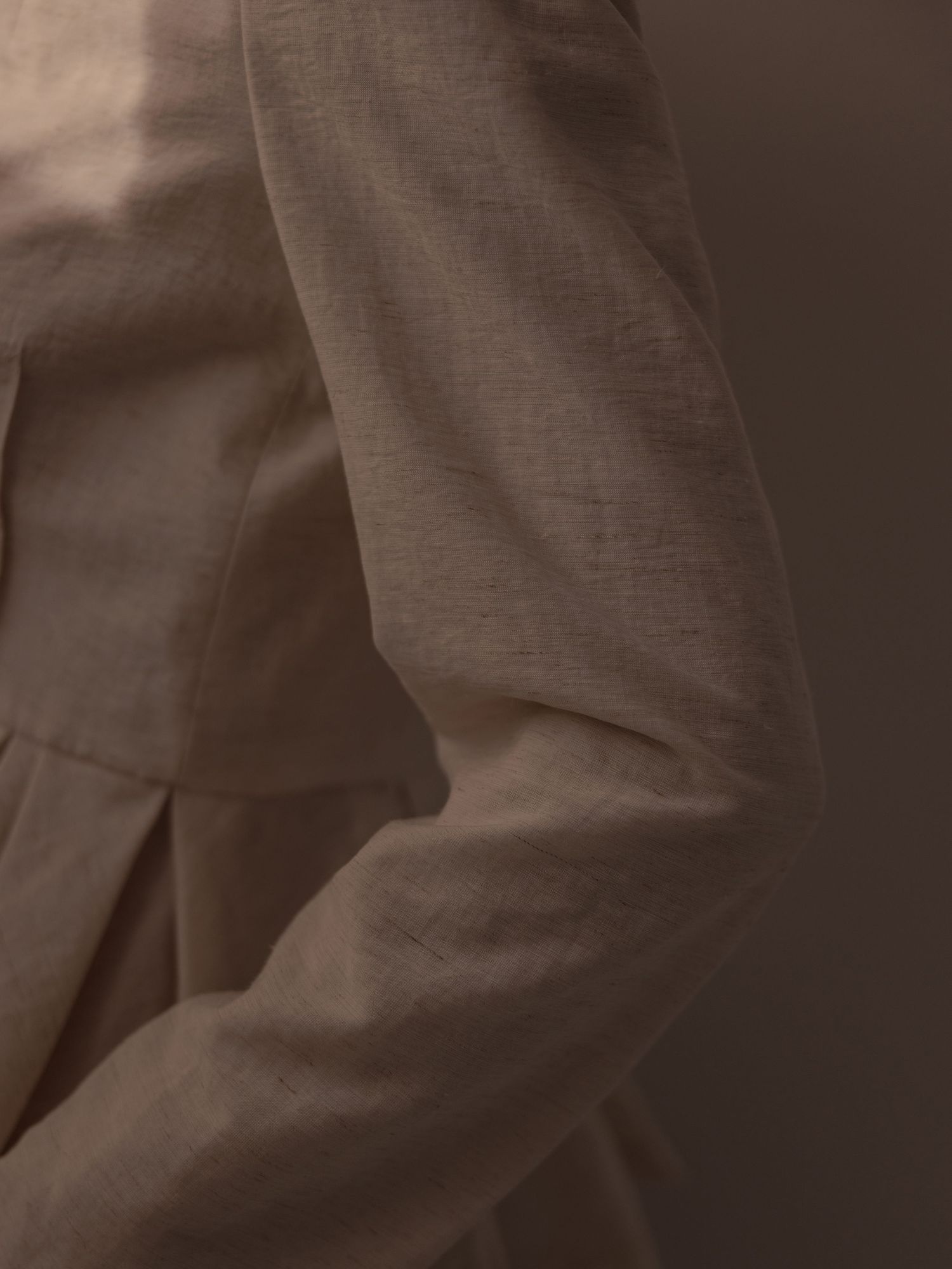 Close-up detail of a taupe linen blazer showing pleated fabric and natural texture.