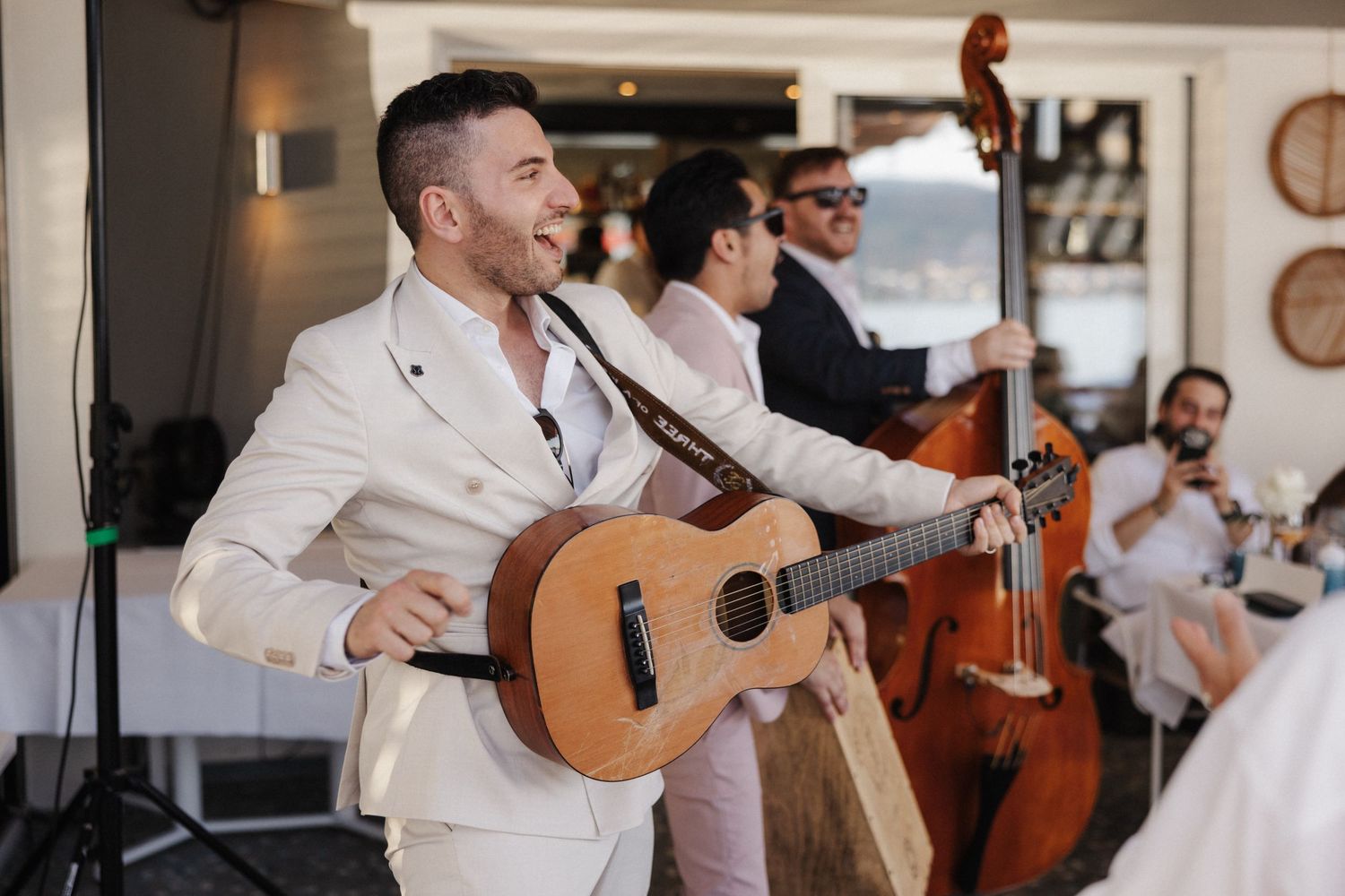 A musician in a white suit performs guitar at an elegant indoor wedding reception.