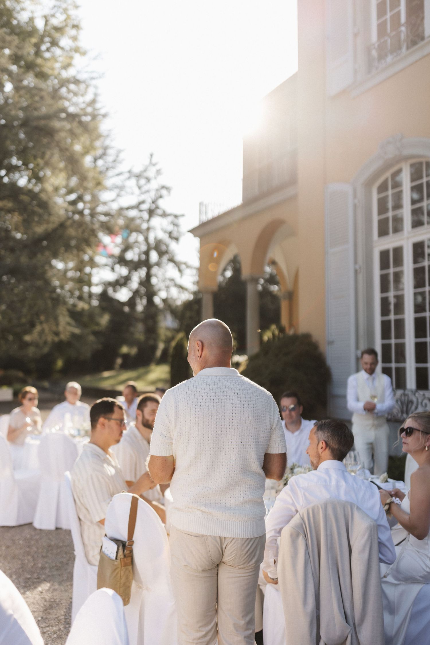 Wedding guests gathered outside an elegant venue in white attire during a golden hour reception.