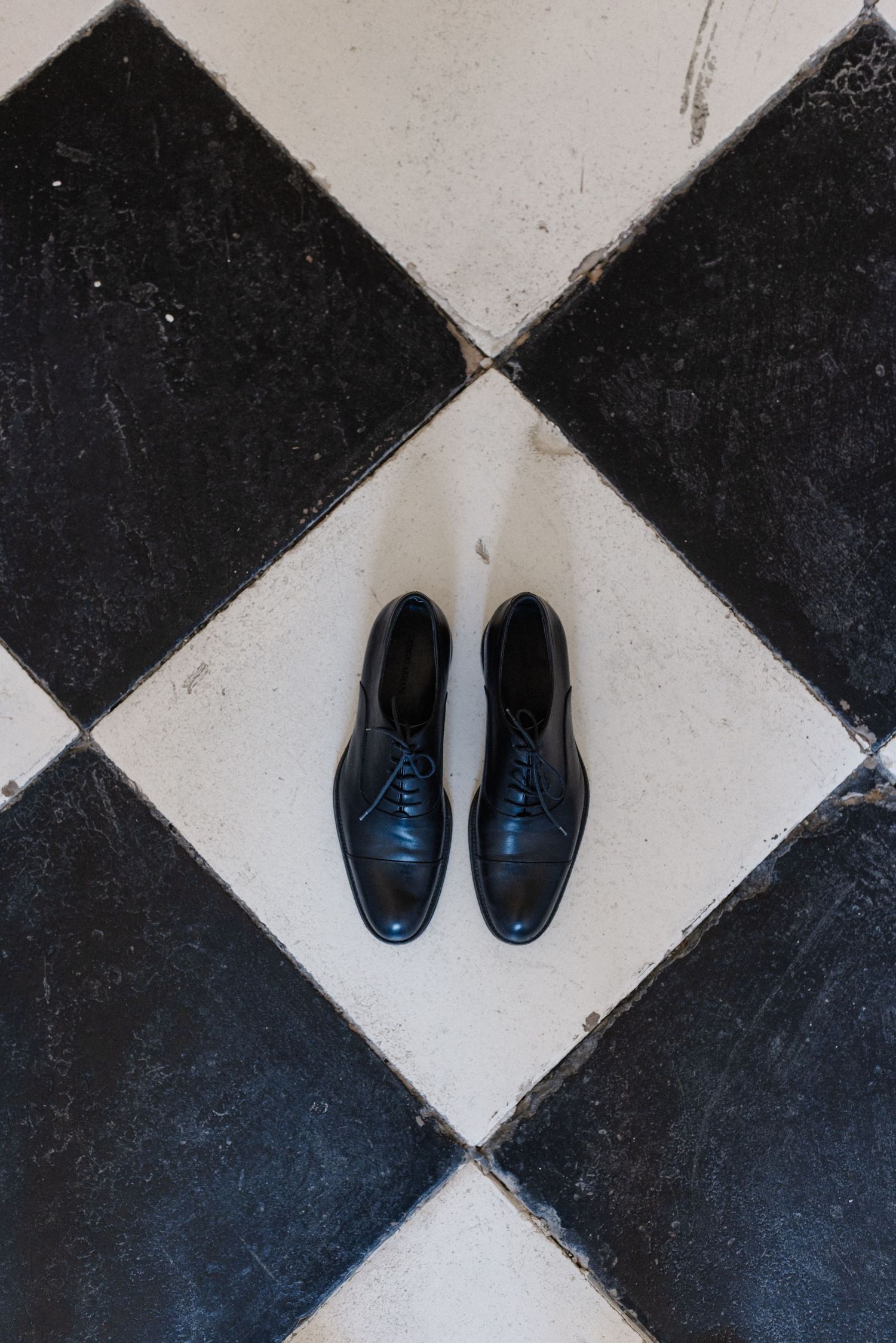 Black leather lace-up dress shoes placed on a classic black and white checkered tile floor.