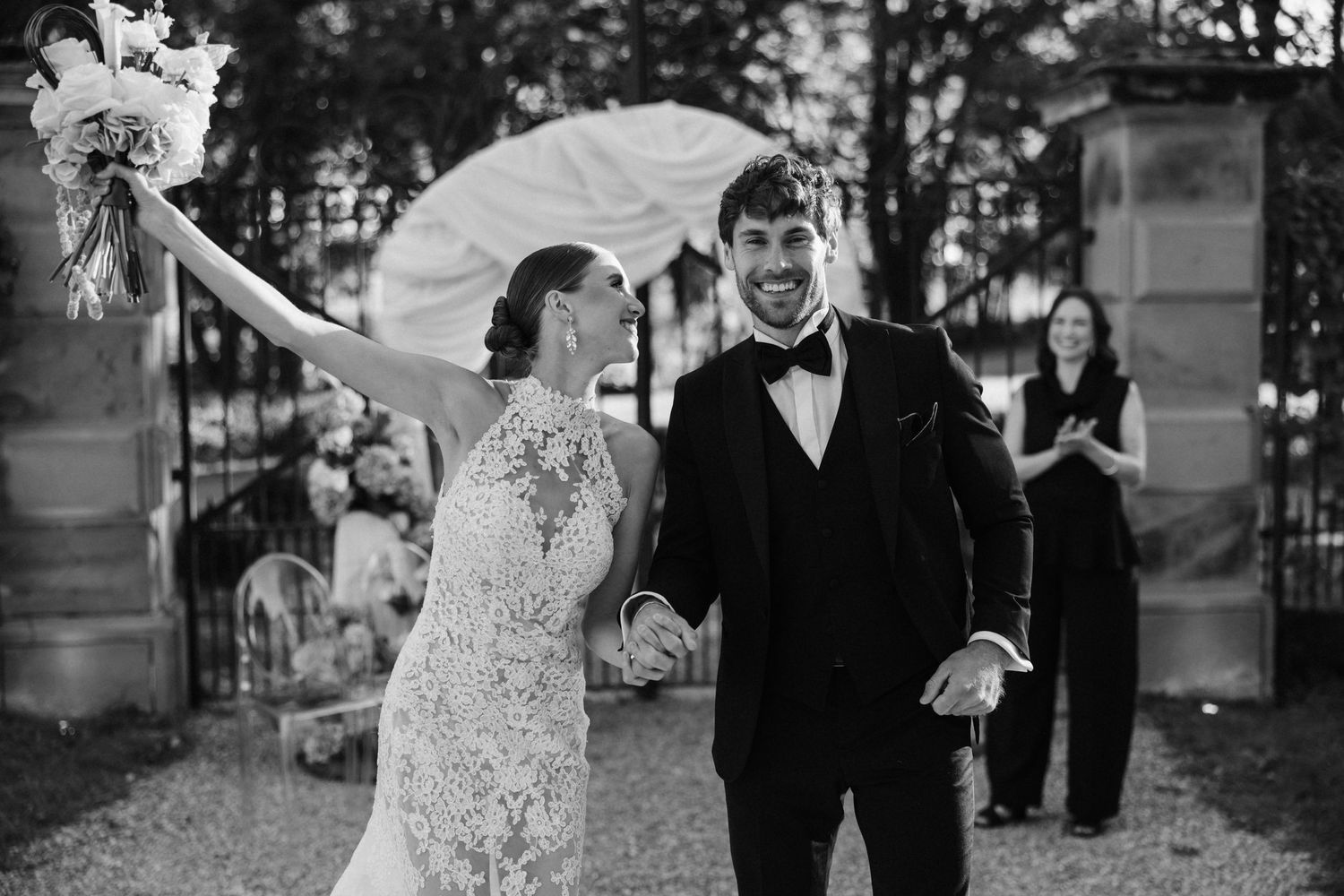 Joyful newlyweds hold hands and celebrate after their outdoor wedding ceremony in black and white.
